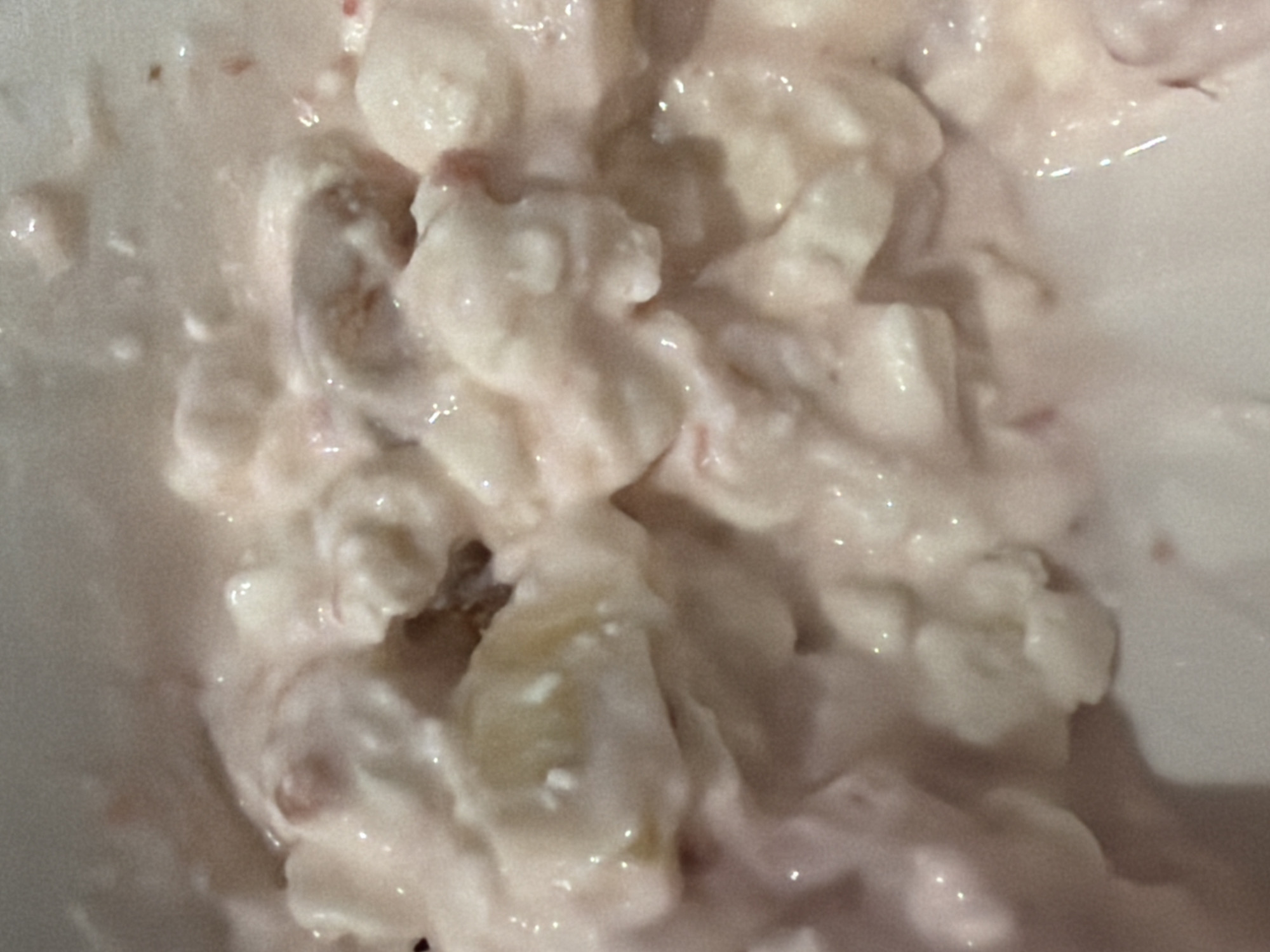 The image shows a close-up of a food item in a bowl. The food consists of small, lumpy pieces coated in a creamy, slightly pink sauce. Some of the pieces appear to be fruit. The scene does not provide any information about the location in Chaikovsky, Russia.