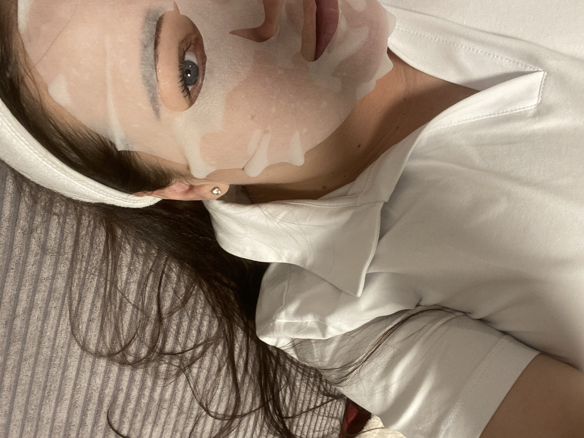 A woman is lying on her back, wearing a white face mask and a white shirt. She has long, dark hair and is wearing a white headband. She is lying on a gray, striped surface. No elements in the image suggest it was taken in Sochi, Russia.