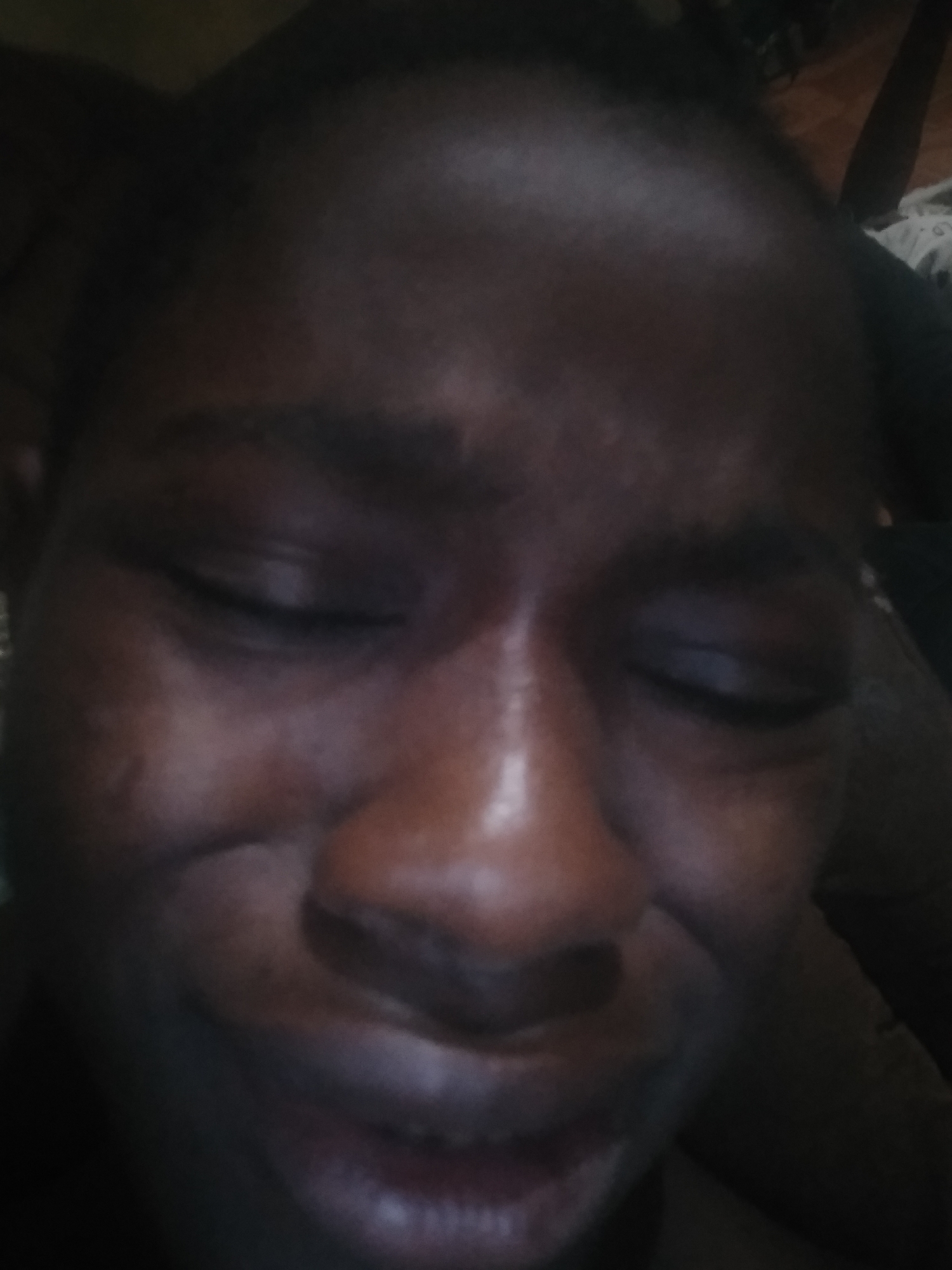 Close-up portrait of a dark-skinned person with eyes closed. The location is unknown.