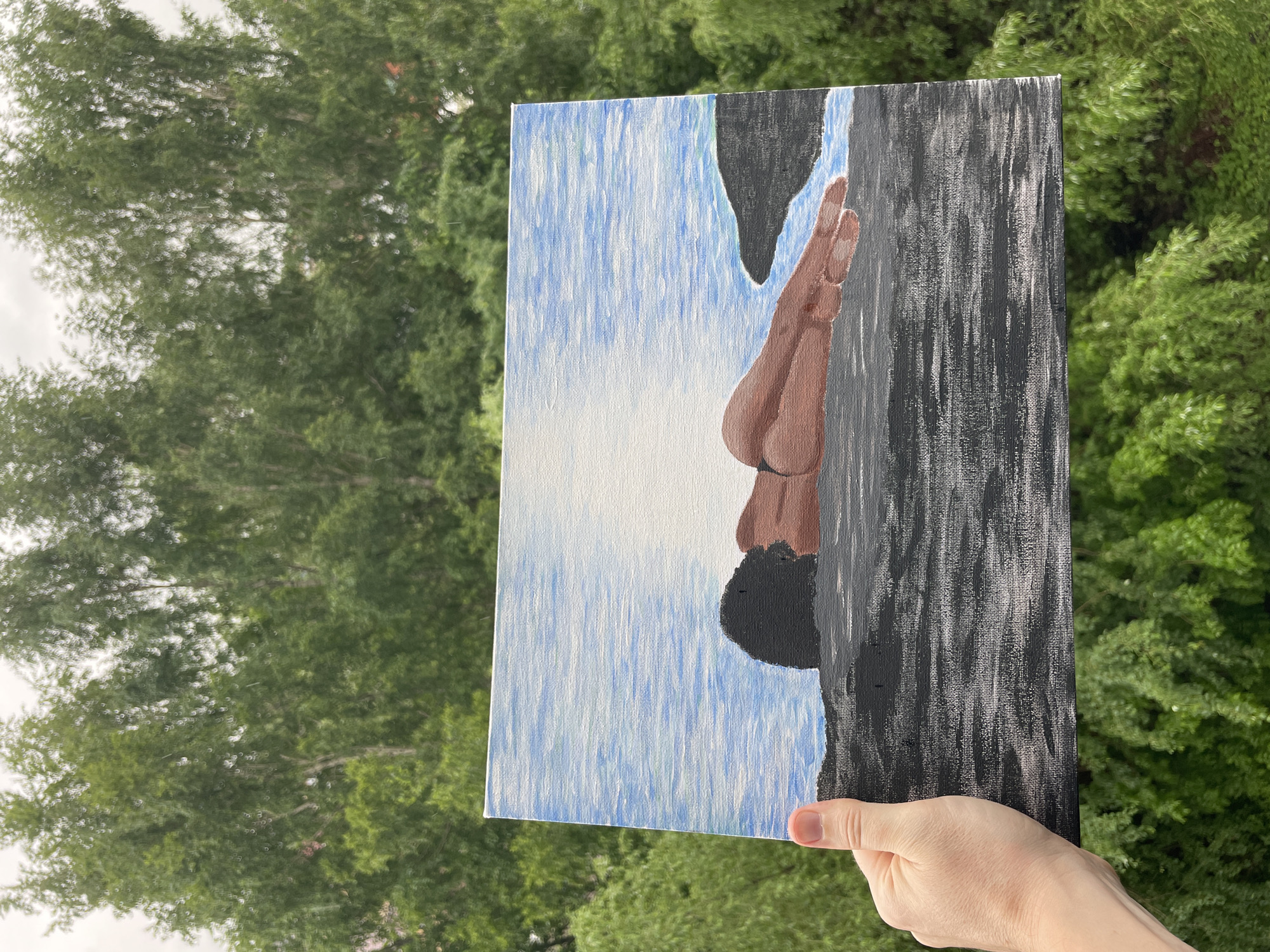 A person holds an acrylic painting in front of an out-of-focus background of green trees, likely outdoors. The painting depicts a figure in mid-dive, transitioning from a dark rock formation on the right to a blue sky with a bright, white central area, suggestive of sunlight, on the left. The figure is dark-skinned with short, black hair. The subject and location of the painting, or its connection to Kazan, Russia, cannot be identified from the image.
