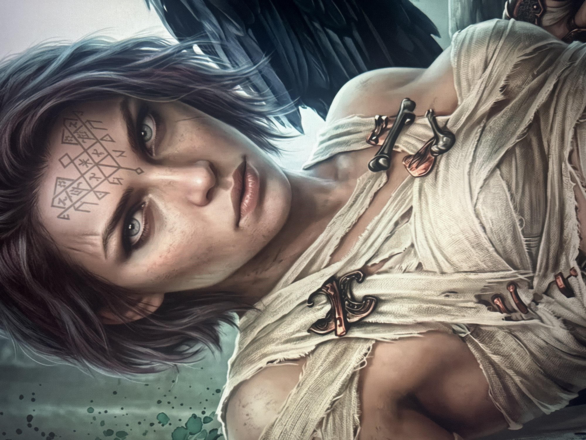 The image is a close-up, digital rendering of a woman with dark hair and striking blue-gray eyes. She has intricate geometric tattoos on her forehead. Her skin is fair and appears weathered, with visible scratches and dust. She is wrapped in torn, off-white bandages that expose her shoulders and chest, held in place by bronze-colored brooches resembling stylized animals or birds. To her right, a large, dark feather, likely from a wing, is visible. The background is a mottled green and gray, with speckles that suggest a textured or painted surface. The overall aesthetic is one of a fierce, possibly warrior or mystical, character. The image does not contain any elements or context that would allow for its localization to Dondușeni, Moldova.