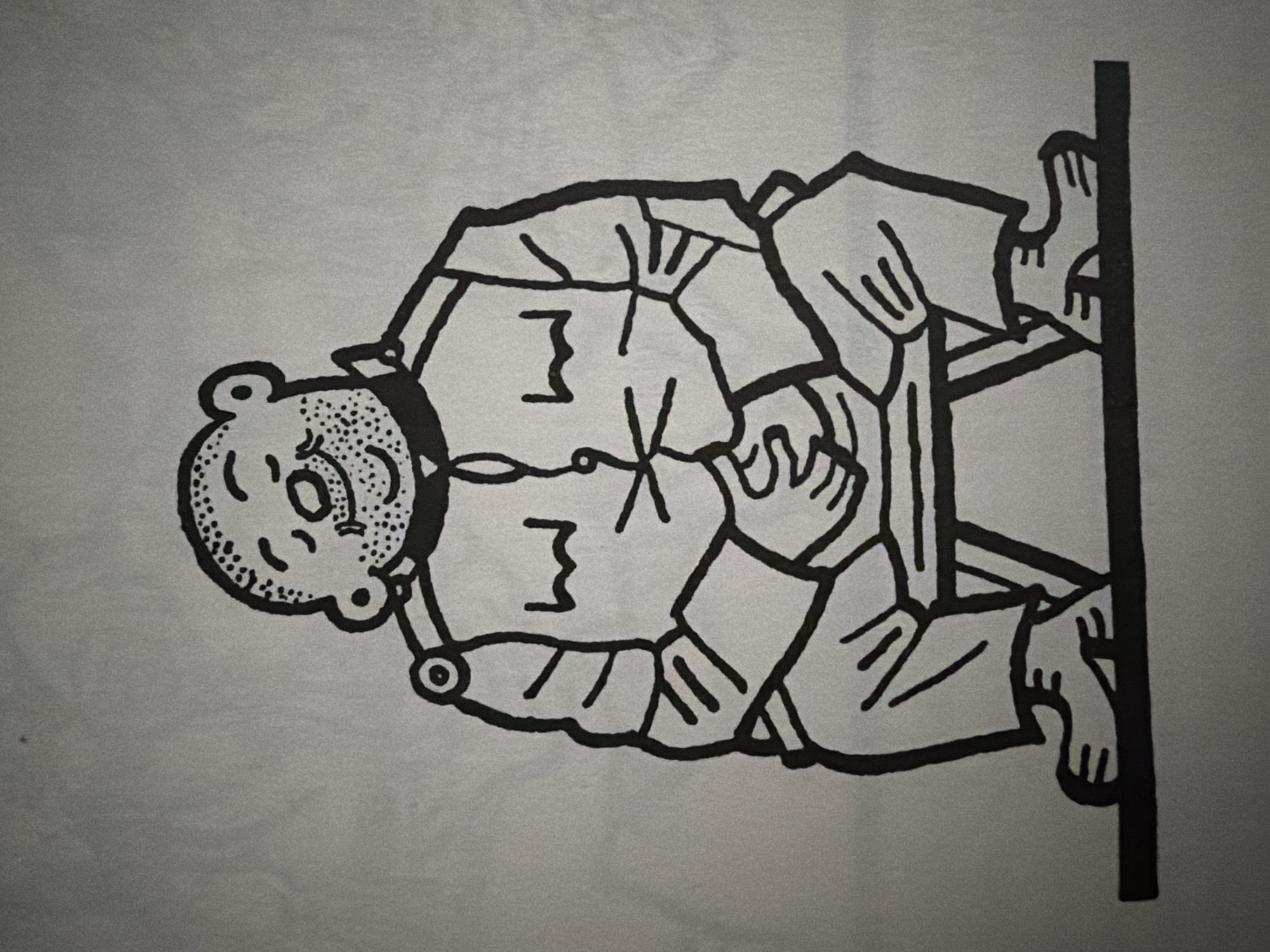 This is a black and white line drawing of a man sitting on a stool. He is bald with a speckled beard and eyebrows, and his eyes are closed as if he is smiling or content. He is wearing a jacket with large lapels and buttons down the front, and appears to be wearing pants. His hands are clasped together in his lap. The stool is a simple, geometric design with legs. The drawing is set against a plain, light gray background. There is no indication of a specific location in Pazardzhik, Bulgaria.