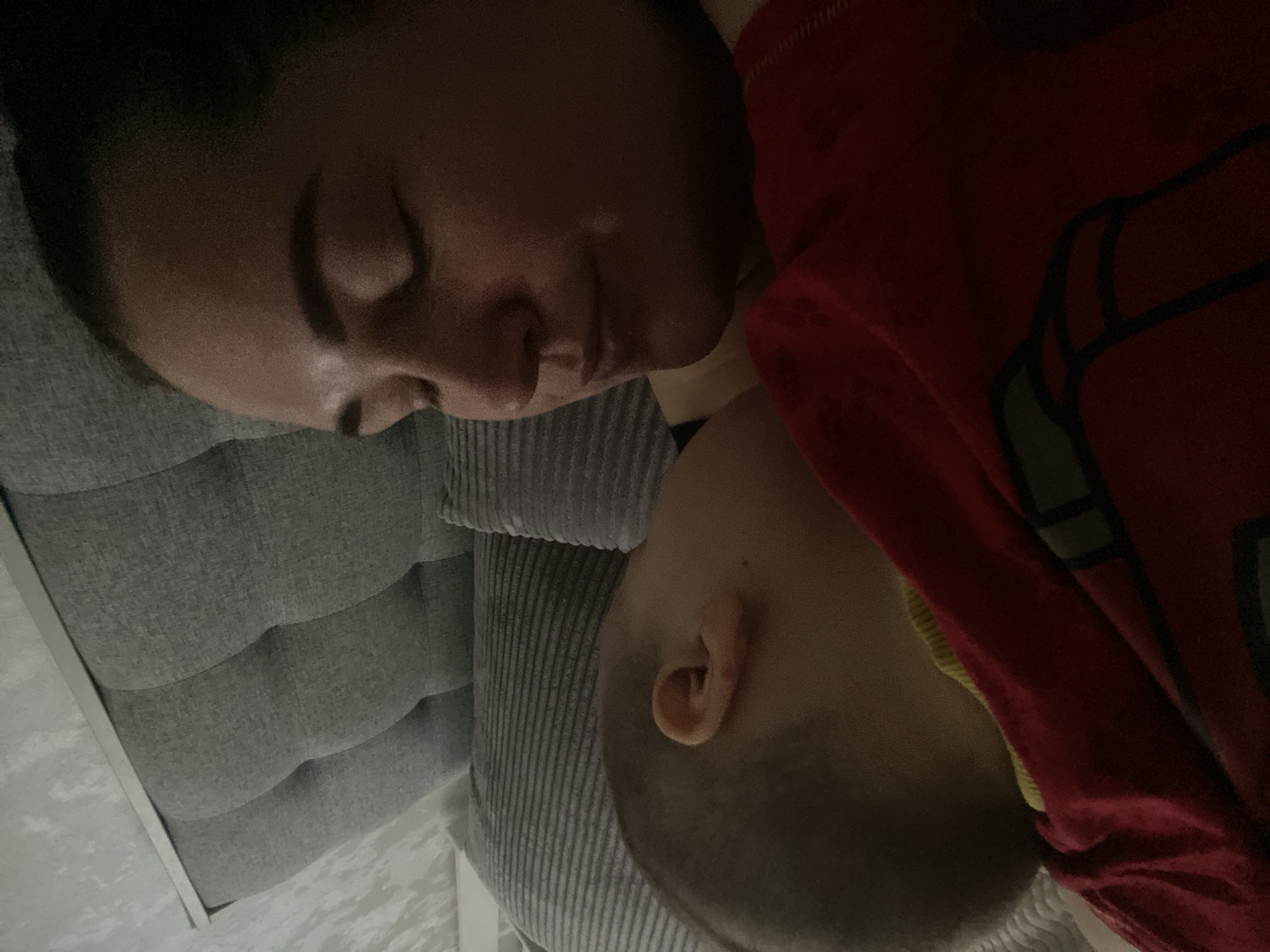 A woman and a child are sleeping on a gray upholstered headboard. The child is wearing a red shirt. The image provides no information about Sochi, Russia.