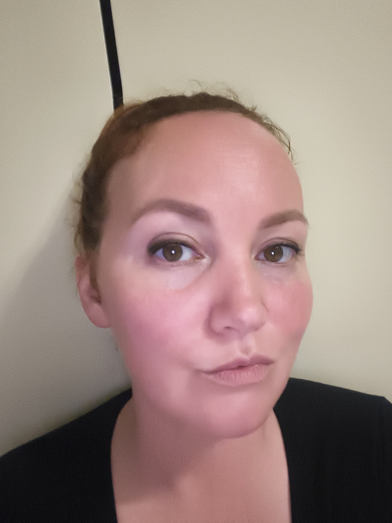 A woman with red hair and fair skin is looking directly at the camera. She has brown eyes and is wearing makeup, including blush, eyeshadow, and lipstick. Her hair is pulled back. She is wearing a black shirt. The background is a plain, light-colored wall. The image was taken indoors, likely in a home or studio setting. No specific location within Chaikovsky, Russia, is discernible from the image itself.