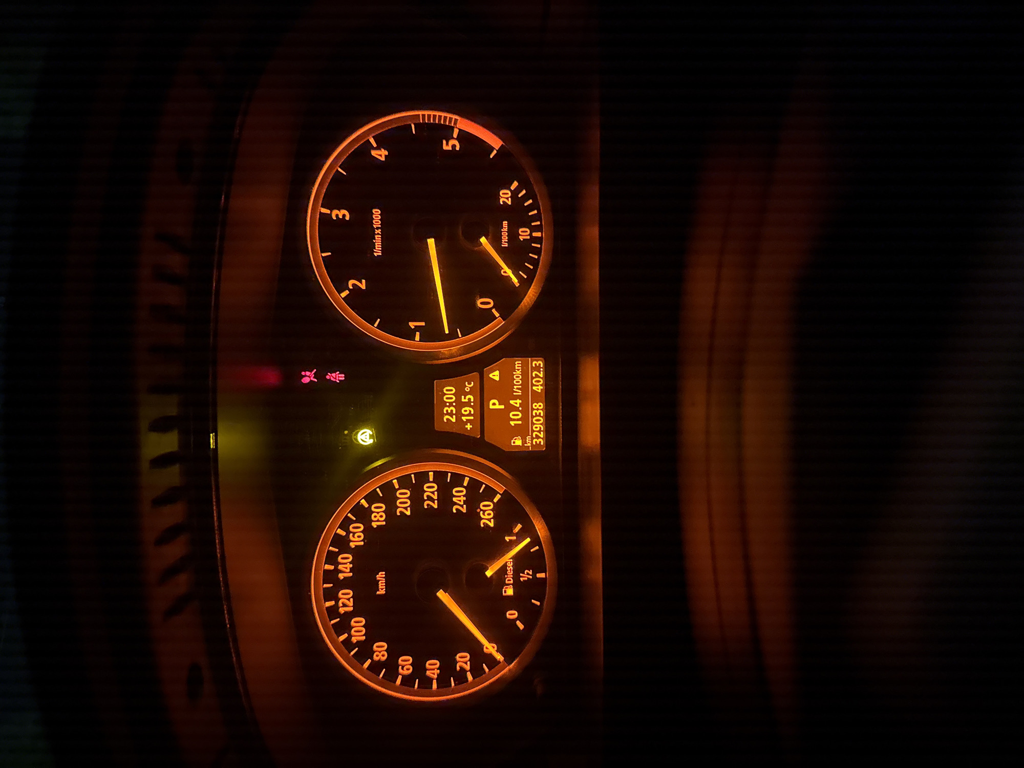 The image shows a car dashboard at night. The speedometer reads approximately 20 km/h. The tachometer reads approximately 0.8 x 1000 rpm. The digital display shows the time as 23:00, a temperature of +19.5°C, the car in "P" (Park), fuel consumption of 10.4 l/100km, total mileage of 329038 km, and trip mileage of 402.3. The fuel gauge indicates it is nearly full with label "Diesel". Location is not discernible from the dashboard image. There is nothing to indicate that the picture was taken in Stara Zagora, Bulgaria.