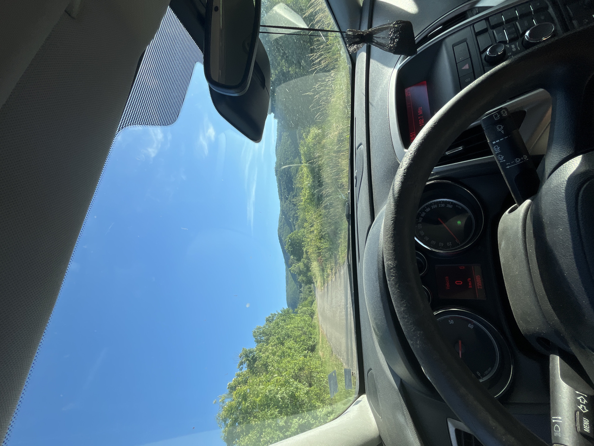 The image is a driver's perspective from inside a vehicle traveling on a road surrounded by lush greenery and mountains in the distance. The speedometer reads 0 km/h, and the odometer shows 235805. The radio is tuned to 102.7 MHz. The location is Granitsa, Bulgaria.