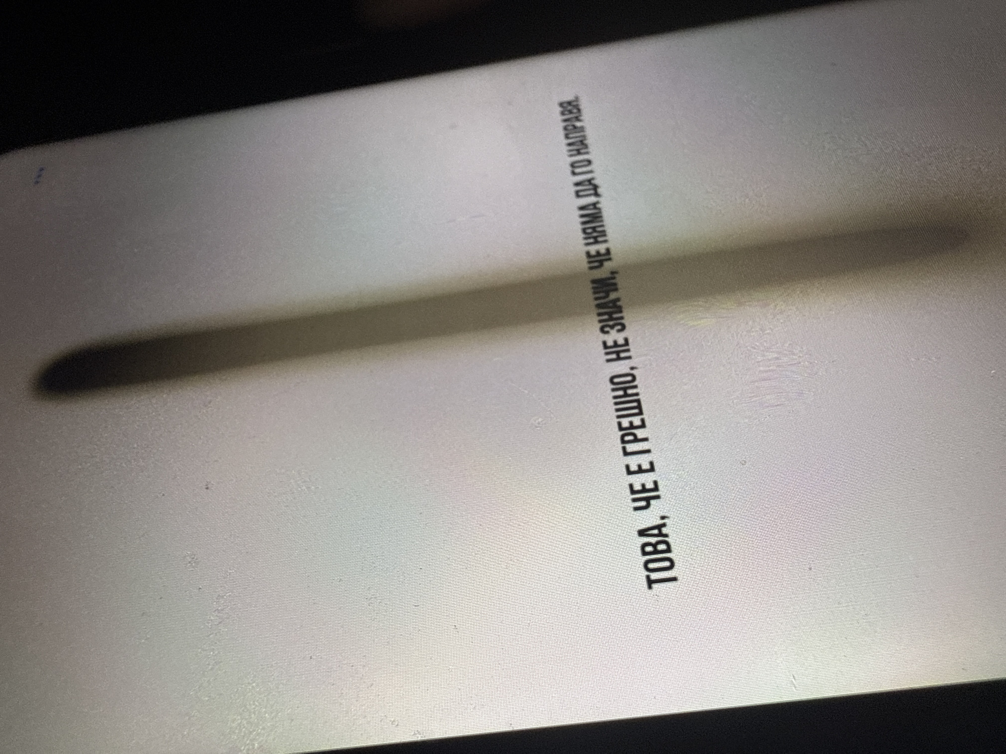 The image is a close-up, oblique shot of a screen displaying text in Bulgarian. The text reads "ТОВА, ЧЕ Е ГРЕШНО, НЕ ЗНАЧИ, ЧЕ НЯМА ДА ГО НАПРАВЯ". This translates to "Just because it's wrong, doesn't mean I won't do it." The screen has a textured surface, and a vertical shadow is cast across it, obscuring some of the text. The background is dark, suggesting the image was taken in a dimly lit environment. There is no discernible location in Sofia, Bulgaria, or any specific environmental context visible in the image.