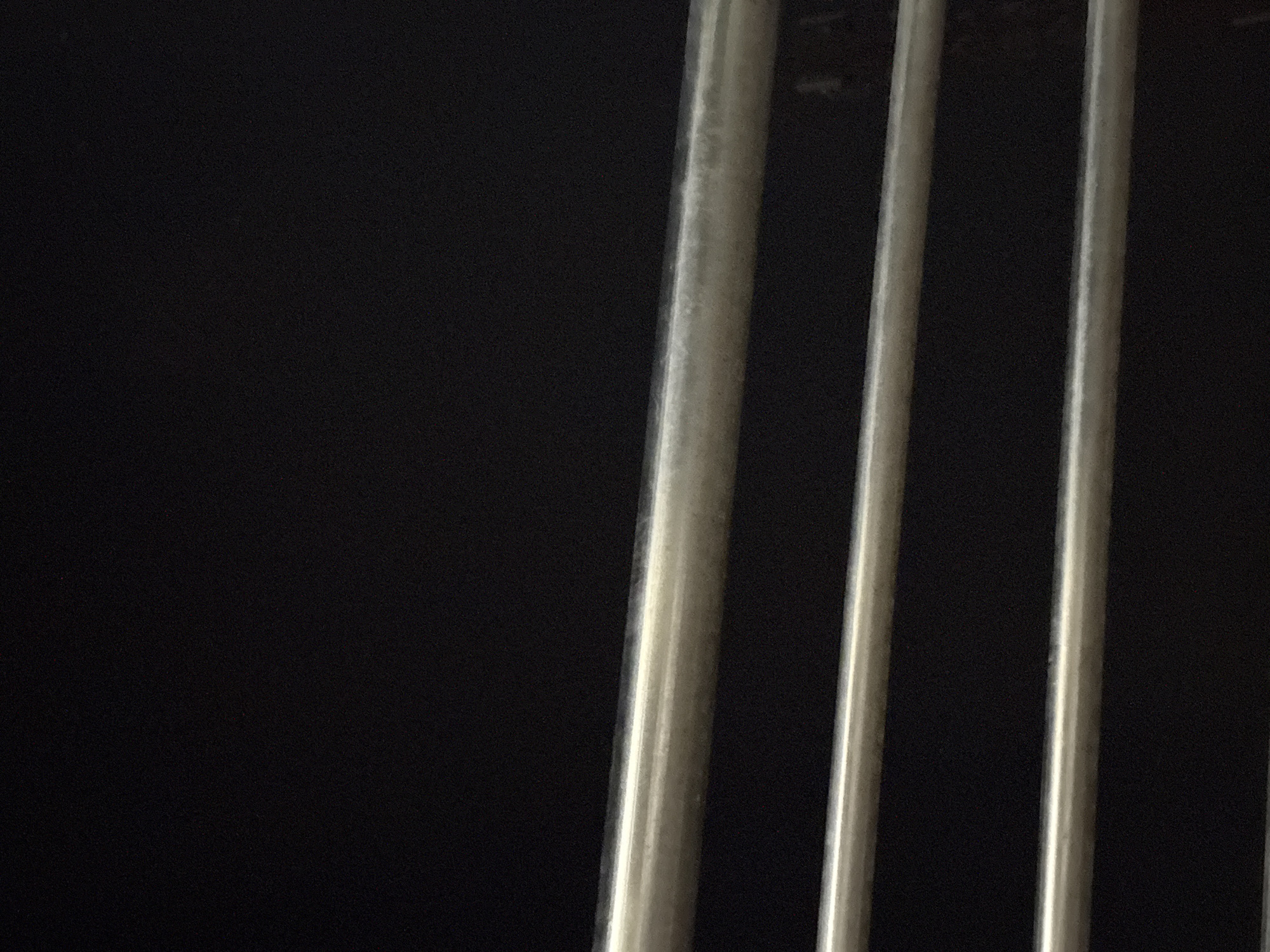 The image shows a close-up, low-angle shot of three horizontal metal bars against a black background. The bars appear to be part of a railing or grate. The lighting is dim, with some reflections visible on the surfaces of the bars. The scene does not provide any contextual information that would allow for a determination of its location in Gempol, Indonesia, or any other specific location. No people, actions, or interactions are depicted.