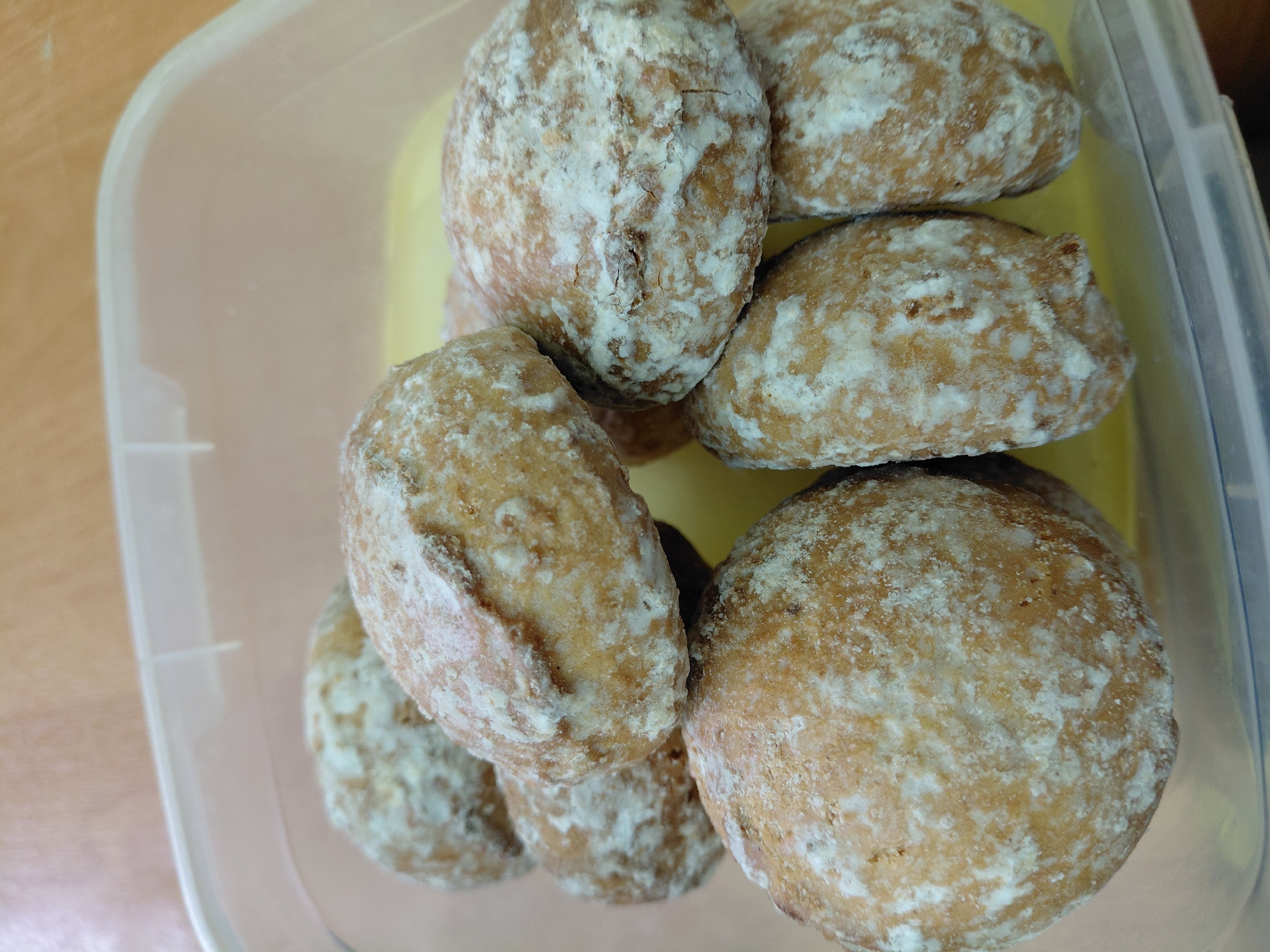 The image shows a plastic container filled with approximately eight gingerbread cookies. The cookies are round to oval-shaped, and coated with a white glaze. The container is transparent, and a yellow object is visible underneath the cookies. The background suggests an indoor setting with a light-colored surface, possibly a table. There is no indication of the specific location in Nadym, Russia, or any people, actions, or interactions.