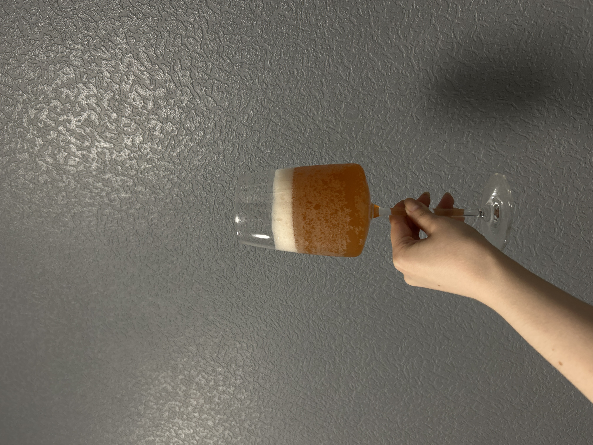 A pale hand holds a glass filled with beer against a textured gray background, likely a wall, in an indoor setting. No specific details confirm the location as Saint Petersburg, Russia.