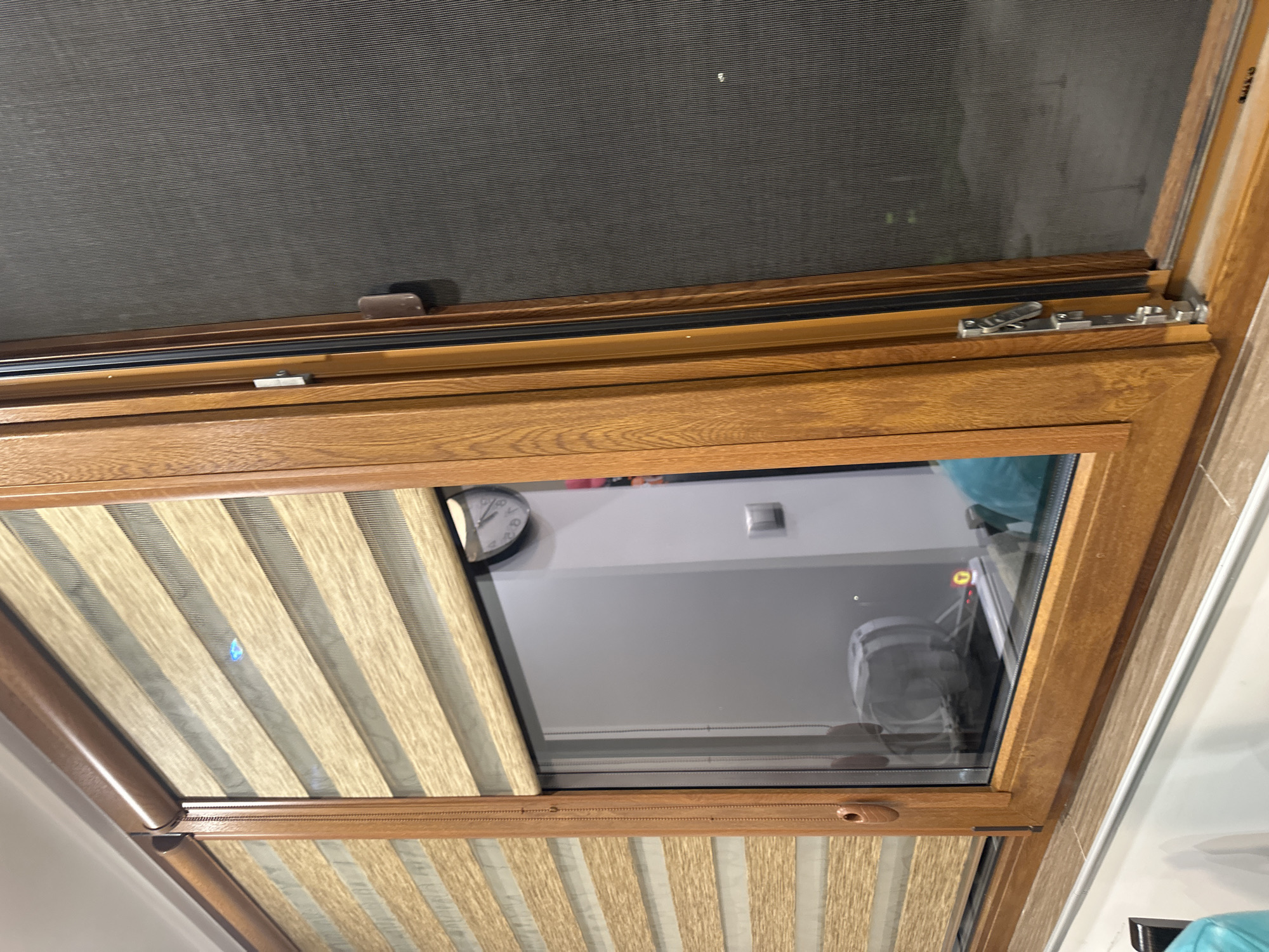 The image shows a close-up view of an open window in a building. The window has a wooden frame and is fitted with blinds. A clock is visible through the window along with the interior of a room. Based on the location information, this is likely in Lovech, Bulgaria.