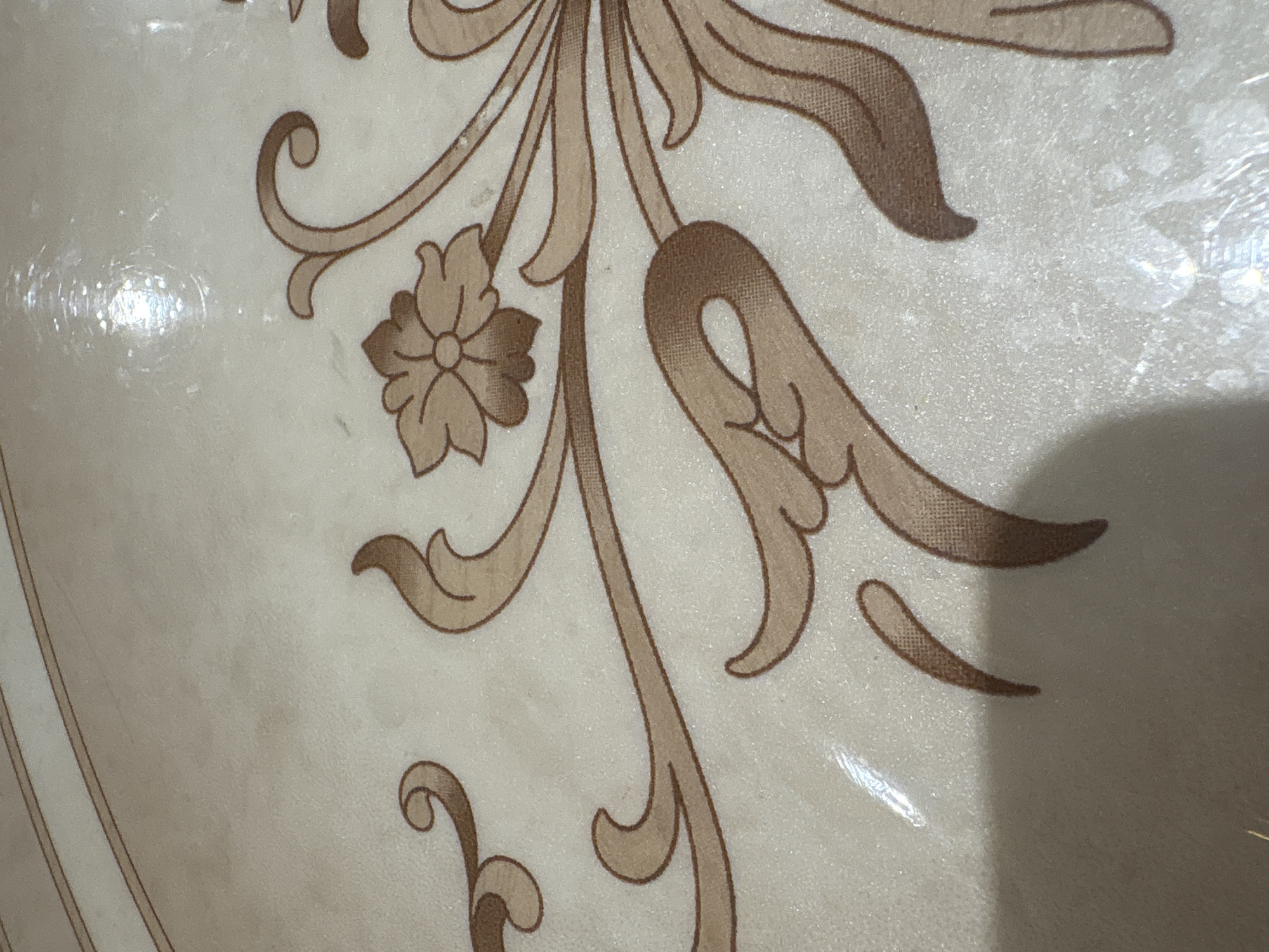 The image shows a close-up of a floral design on a surface. The design consists of stylized leaves and flowers in shades of brown and beige. The background appears to be a light beige or cream color. The surface may be shiny or have a glossy finish. The scene is not identifiable as being located in Chaikovsky, Russia or any other specific location.