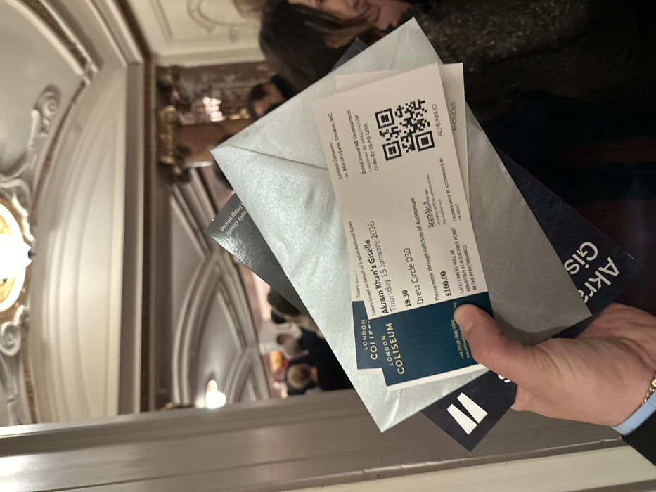 A hand holds tickets for "Akram Khan's Giselle" at the London Coliseum on Thursday, January 15, 2026, at 19:30. The seat is in Dress Circle D30, priced at £100.00. One ticket has a QR code and order information. The London Coliseum address is St. Martin's Lane, London, WC. The text advises latecomers will be admitted at a suitable point, and children must be accompanied by an adult. A partial program is included with the tickets.