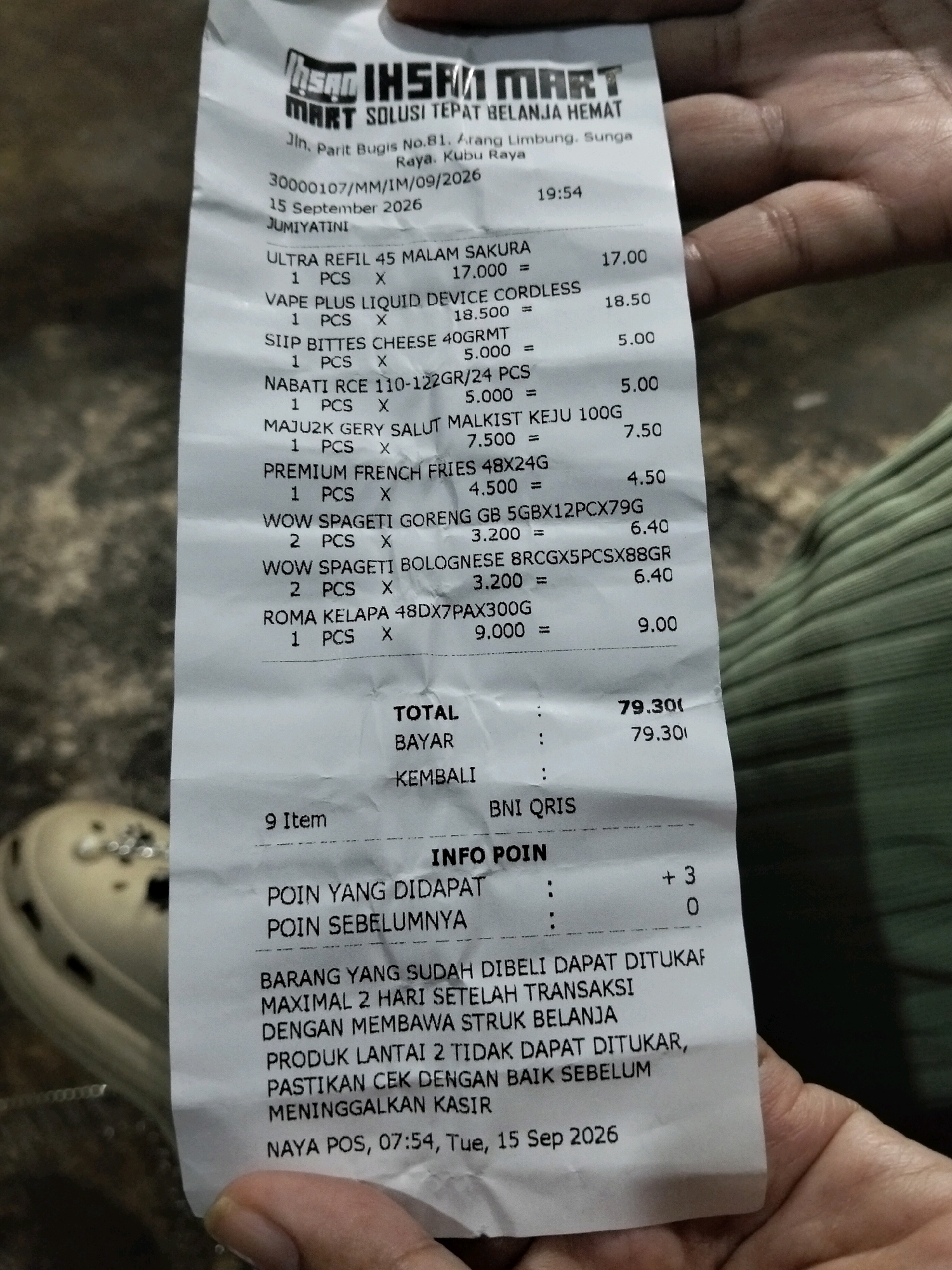 The image shows a receipt from IHSAH MART. The receipt is from Jln. Parit Bugis No.81, Arang Limbung, Sungai Raya, Kubu Raya, Indonesia, dated September 15, 2026, at 19:54. It lists several items purchased, including "ULTRA REFIL 45 MALAM SAKURA", "VAPE PLUS LIQUID DEVICE CORDLESS", "SIIP BITTES CHEESE 40GRMT", "NABATI RCE 110-122GR/24 PCS", "MAJU2K GERY SALUT MALKIST KEJU 100G", "PREMIUM FRENCH FRIES 48X24G", "WOW SPAGETI GORENG GB 5GBX12PCX79G", "WOW SPAGETI BOLOGNESE BRCGX5PCSX88GR", and "ROMA KELAPA 48DX7PAX300G". The total amount is 79.30. The receipt also indicates "BNI QRIS" as the payment method. Below this, there is a section for "INFO POIN" which states "POIN YANG DIDAPAT" and "POIN SEBELUMNYA". Further down, there is a notice about returning items and a date of "NAYA POS, 07:54, Tue, 15 Sep 2026". The image is taken from a close-up perspective, with a person's hand visible in the foreground and background, partially obscuring parts of the receipt.