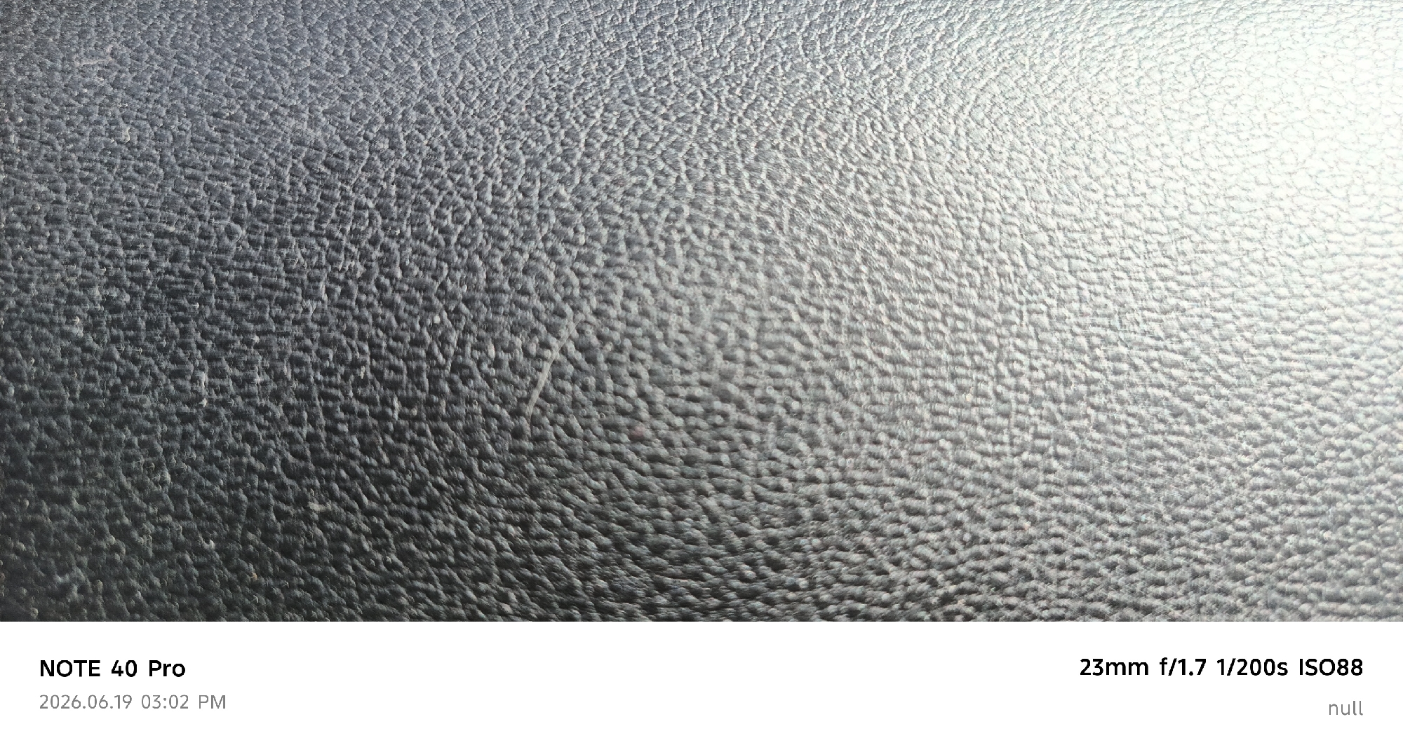 The image is a close-up, macro photograph of a textured, dark gray surface, possibly leather or a similar synthetic material, exhibiting a repeating pattern of small, raised bumps or dimples. The lighting creates subtle highlights and shadows that accentuate the texture. The bottom of the image contains overlaid text: "NOTE 40 Pro 2026.06.19 03:02 PM 23mm f/1.7 1/200s ISO88 null." There are no people or discernible environmental elements of Buzovna, Azerbaijan in this image.