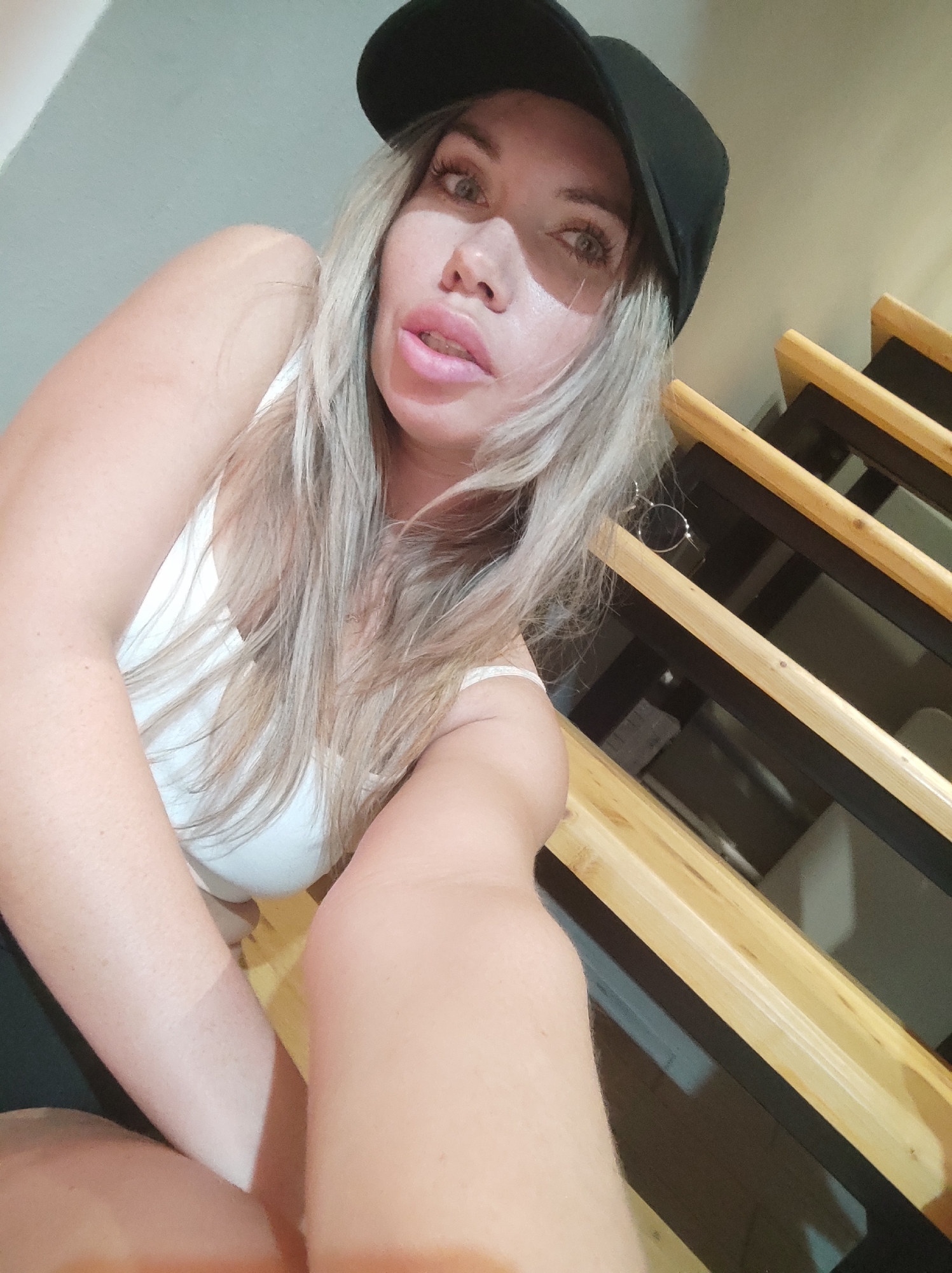 A woman wearing a black baseball cap and white tank top sits on wooden stairs. The location is unidentifiable as Votkinsk, Russia.
