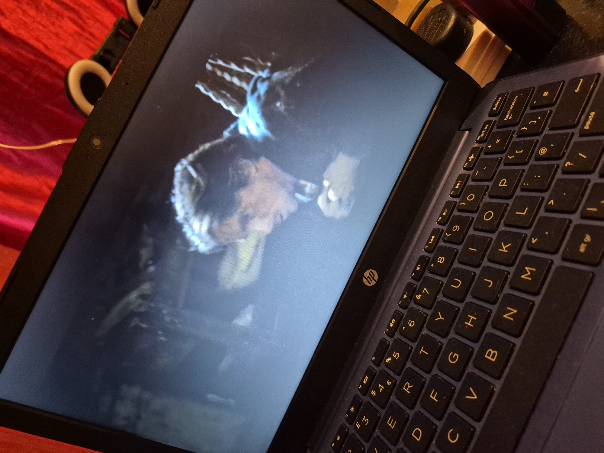 A close-up, angled shot shows an open laptop computer displaying a movie scene. The movie appears to be a drama, with a man in the foreground looking down and to the left, his hands clasped. He is wearing dark clothing. The background of the movie is dark and appears to be an indoor setting. The laptop's keyboard is visible, with dark keys and yellow lettering. The HP logo is visible on the keyboard area. The background behind the laptop is out of focus, but appears to be a red fabric surface. The scene is set in Sandwell, United Kingdom.