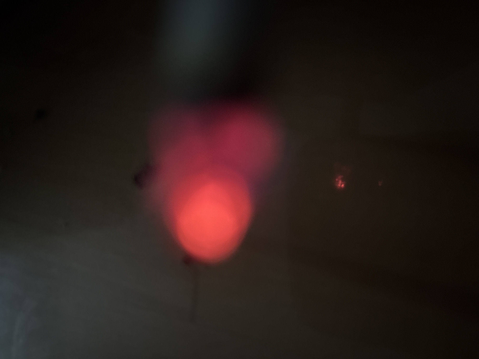 The image is a blurred, dark, and abstract shot featuring prominent red and pink bokeh lights. The lights appear to be concentrated in the center-left of the frame, with a few smaller red specks visible towards the bottom and right. The background is a dark, indeterminate space, possibly an interior or a night scene with limited ambient light. There are no discernible structures, landmarks, or identifiable features that would allow for localization within Plovdiv, Bulgaria, or any other specific city. The image is devoid of any human presence or clear subjects.