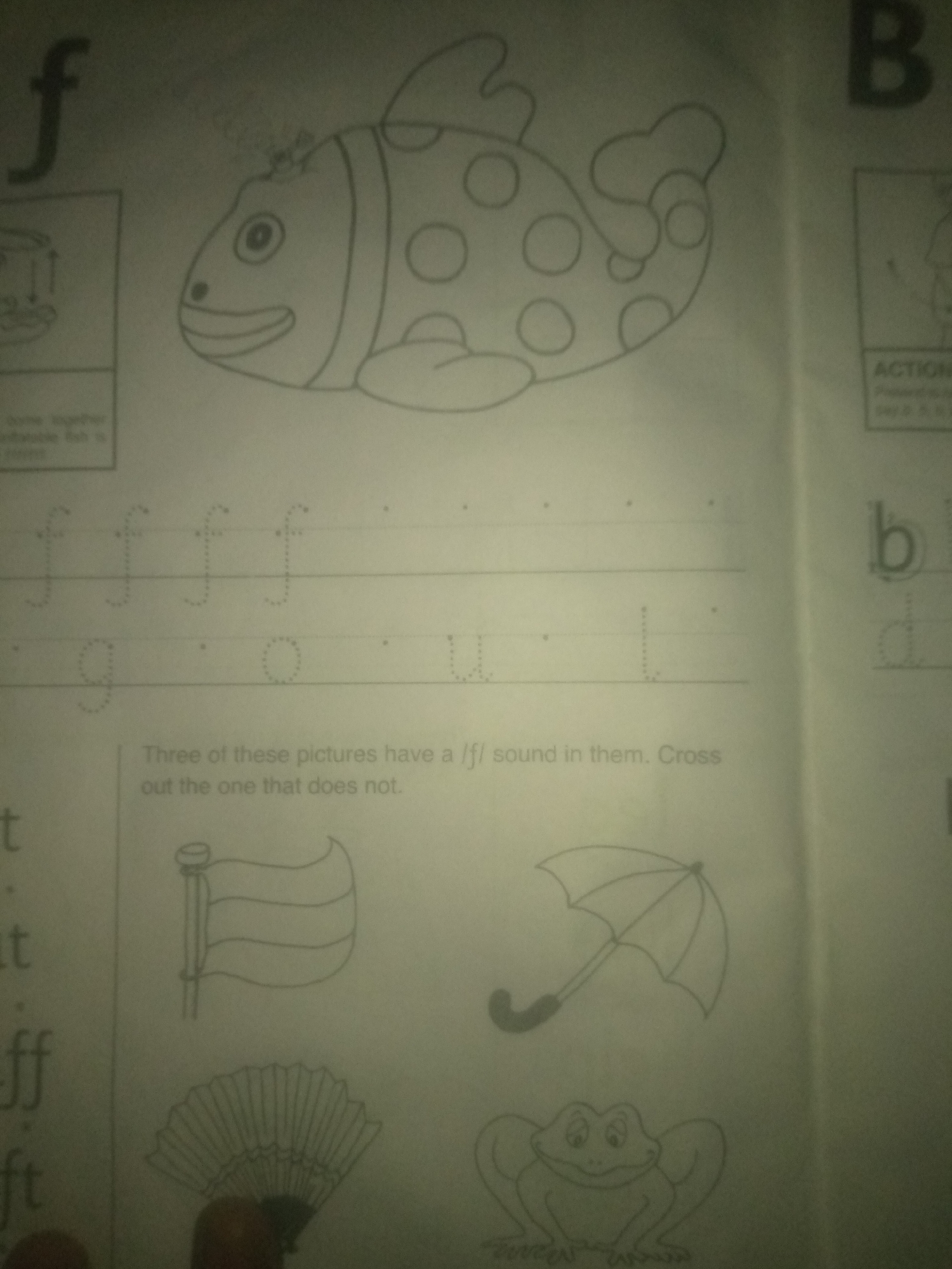 The image shows a page from a children's learning book, likely for practicing letters and sounds. On the left, the letter "f" is prominently displayed in large print, followed by a drawing of a fish with polka dots. Below this, there are dotted outlines of the letter "f" repeated several times, presumably for tracing. Further down, there are dotted outlines of the letters "g", "o", and "u". Below these letters, there is an instruction in text: "Three of these pictures have a /f/ sound in them. Cross out the one that does not." Below this text are three drawings: a flag, an umbrella, and a frog. On the right side of the page, the letter "B" is visible, followed by dotted outlines of the letter "b". The overall environment appears to be an indoor setting with printed educational materials. There is no information or visual context in the image that would allow for the identification of a specific location in Jauro Yinu, Nigeria.
