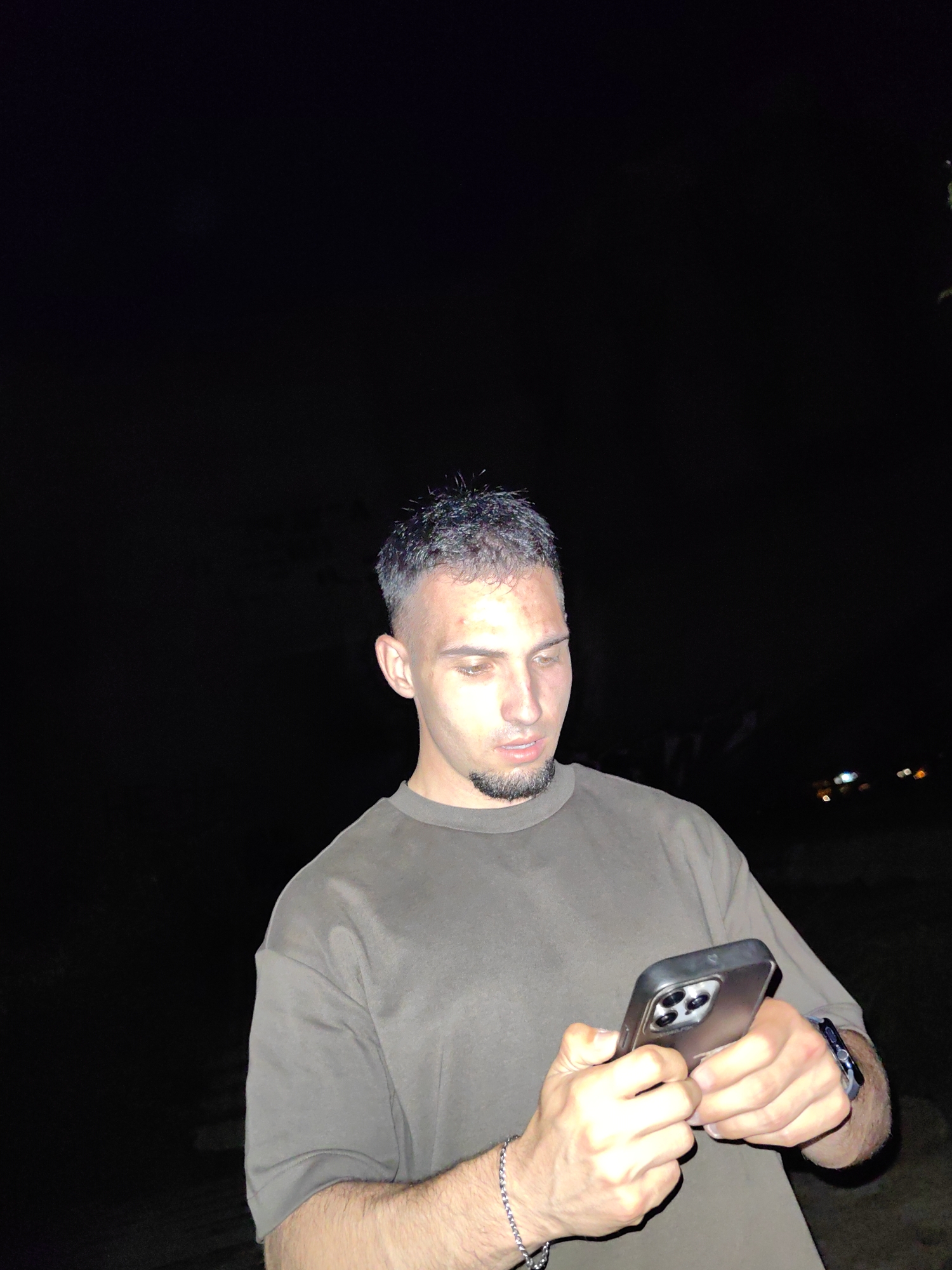 A man is holding a mobile phone. The location is unknown. The background is dark.