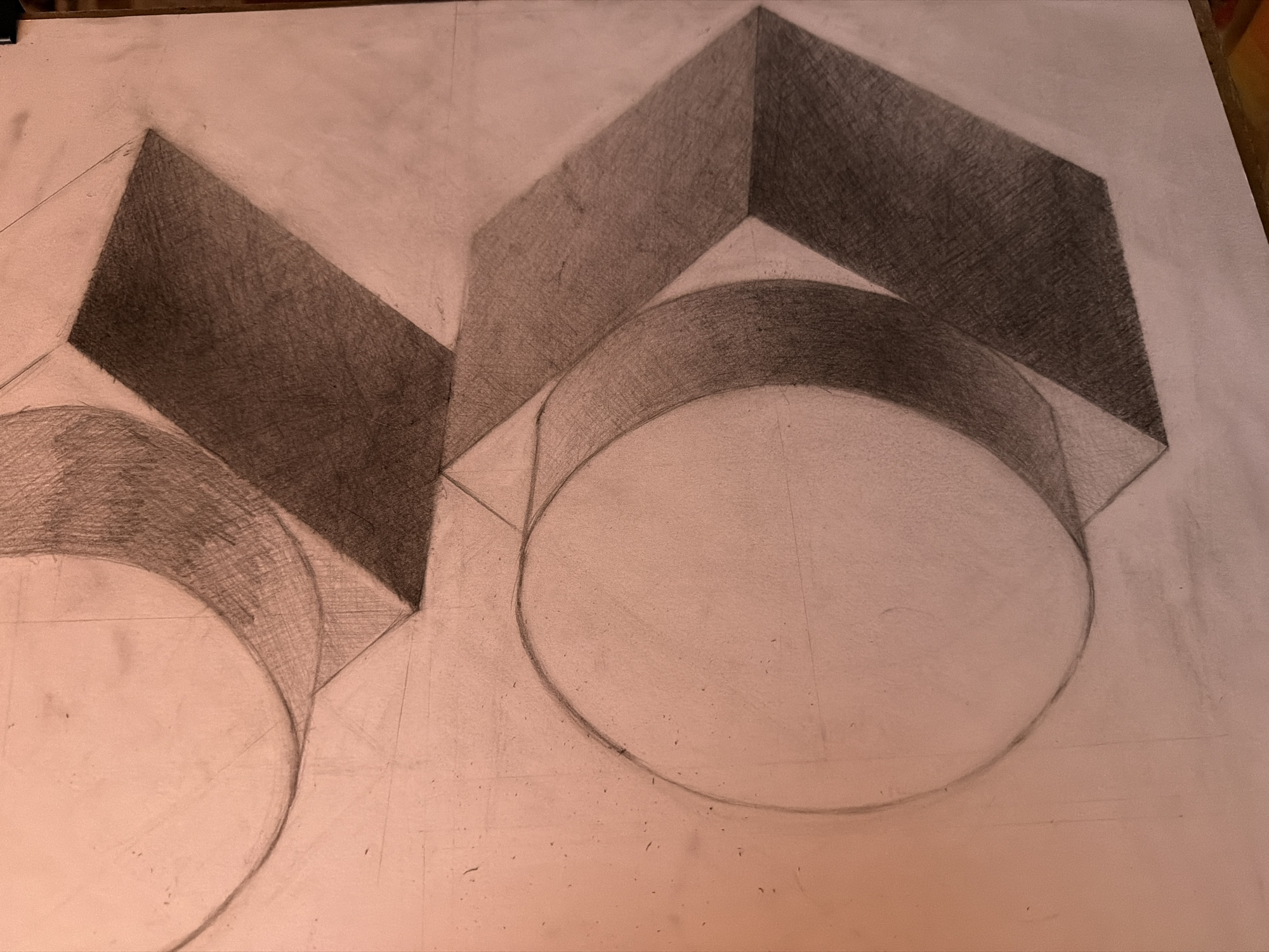 A pencil drawing depicts two geometric forms. Each form consists of a rectangular prism stacked on top of a cylinder. The prism faces are shaded to indicate light and shadow, while the cylinders are outlined. The drawing is on a light-colored sheet of paper. There is no indication this is in Velingrad, Bulgaria. There are no people present.