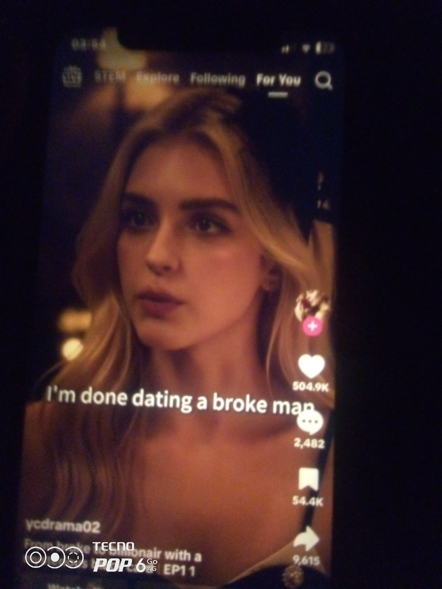 The image is a screenshot of a social media video, likely from TikTok, displayed on a smartphone. The video features a young woman with blonde hair and a light-colored top. Text overlays on the video read "I'm done dating a broke man" and "ycdrama02 From broke to billionaire with a TECNO POP 6 4G EP11". There are also engagement metrics visible, including likes (504.9K), comments (2,482), shares (54.4K), and views (9,615). The phone is dark, suggesting it's being used in a dimly lit environment. The presence of the "TECNO" branding on the phone suggests the user is likely in a region where this phone brand is popular, such as Nigeria. However, there is no visual information in the image to specifically pinpoint the location within Howayi, Nigeria.