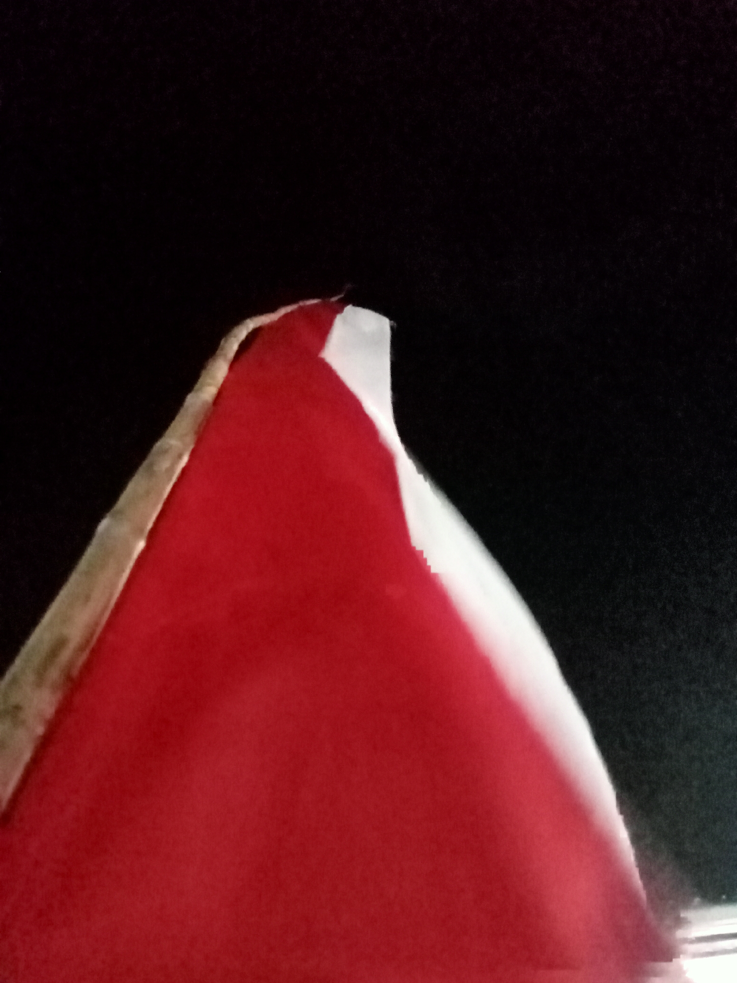 A close-up, low-angle shot of a red object with a white edge against a dark, out-of-focus background. The red object appears to be fabric, possibly part of a flag or banner, with a light-colored edge that is slightly frayed. The lighting is dim and creates a dramatic effect, highlighting the texture of the material. The specific location in Simo, Indonesia is not discernible from the image itself, as it focuses on the abstract qualities of the object and its presentation.