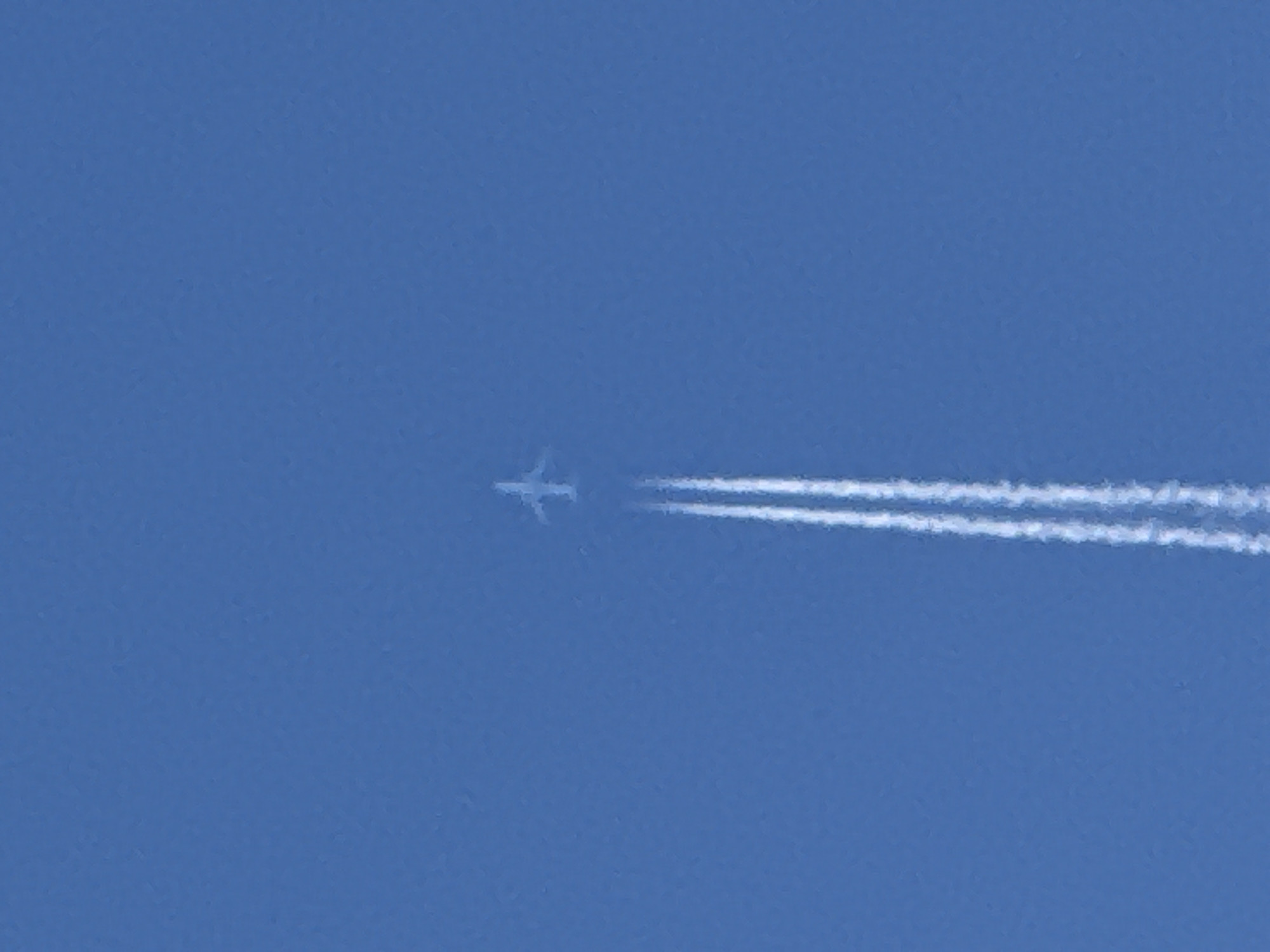 An airplane is visible in a clear blue sky, leaving a contrail. The airplane is small and appears to be in the upper portion of the image. The contrail extends downwards from the airplane, forming two distinct white lines against the blue background. The image does not provide any information or context related to the city of Sozopol, Bulgaria.
