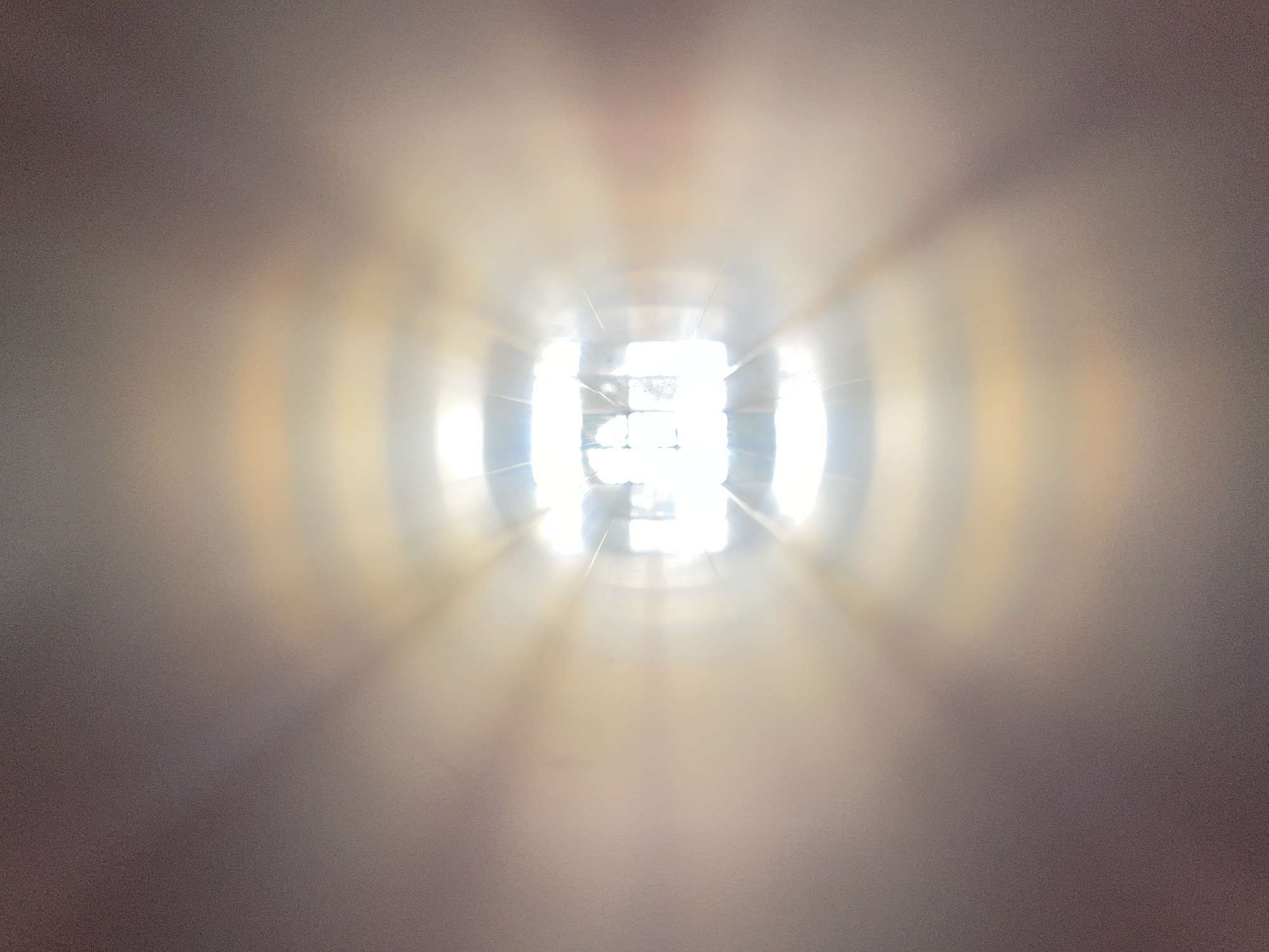 The image depicts a bright light source at the end of a tunnel-like structure. The light appears to be shining through a gridded window. The walls of the tunnel are blurred and appear to be a light gray or beige color. The tunnel structure seems to be made of a smooth material. The light source obscures details about what is beyond the window. The scene is not clear enough to definitively determine a location in Burgas, Bulgaria, but the architecture may be modern.