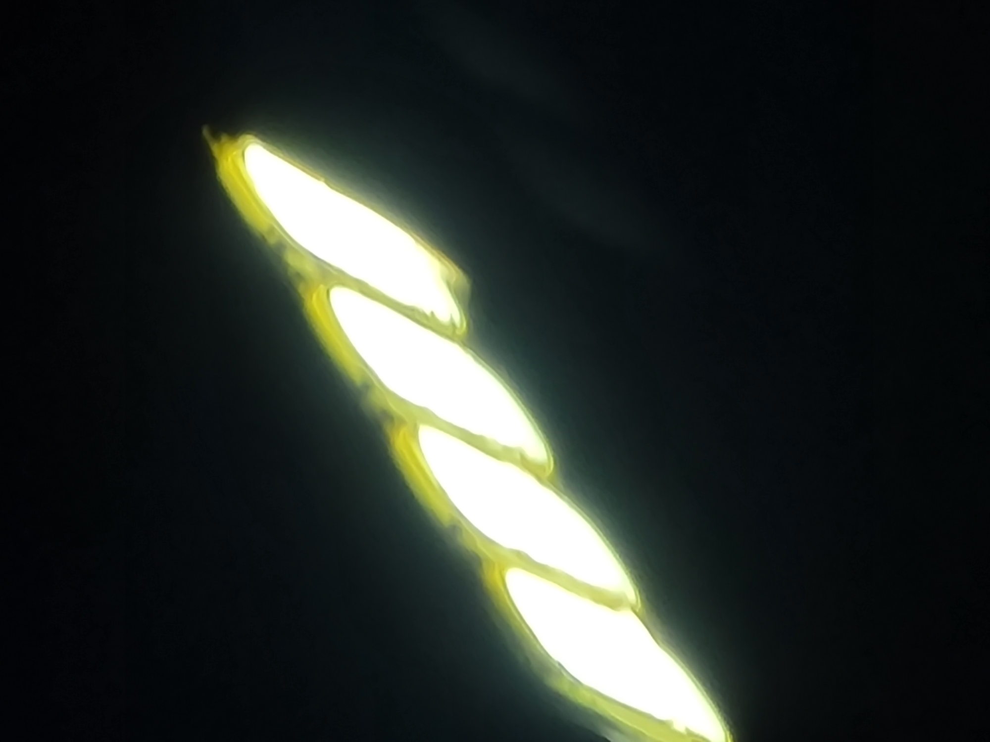 The image shows a bright, elongated object with a twisted, segmented appearance, set against a dark background. The object is luminescent, emitting a bright white and yellow light. The segments are oval-shaped and appear to be fused together, with a swirling pattern visible in the yellow halo surrounding them. The object is positioned diagonally across the frame, extending from the bottom left to the top right. The dark background suggests it is nighttime or a dimly lit environment.
Based on available information, this image likely depicts an LED street lamp. Street lamps in Barakin Akawo, Nigeria, are common fixtures in urban areas, providing illumination for roads and public spaces. The specific design of this lamp, with its segmented, twisted form and bright LED lighting, is consistent with modern street lighting solutions used in many cities. Barakin Akawo, as part of the Jos metropolis in Plateau State, experiences regular power outages, making functional street lighting crucial for public safety and security. The presence of such lamps contributes to the visibility and accessibility of the area after dark, especially in neighborhoods like Barakin Akawo, which is a densely populated residential and commercial district.