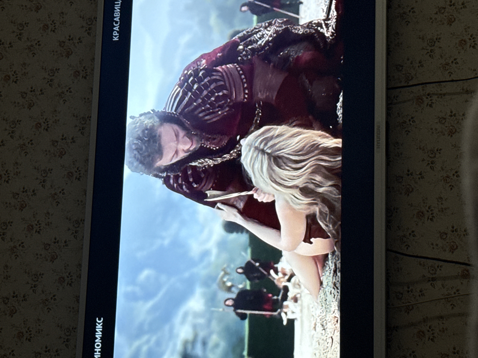 The image shows a scene from the movie "Alice in Wonderland," likely being displayed on a Hyundai TV. The scene features the Queen of Hearts leaning over Alice, who is kneeling and reading a scroll. In the background, several card soldiers are visible. The location in the city of Pushkino, Russia, cannot be determined from the image.
