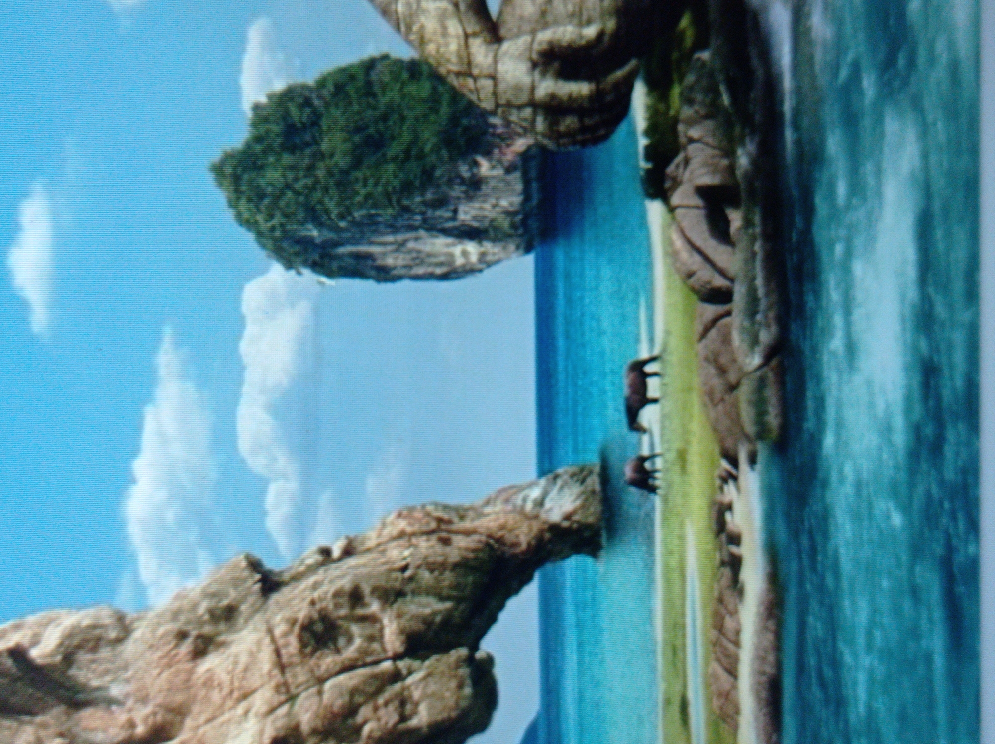 The image depicts a picturesque coastal landscape with a bright blue sky dotted with white clouds. In the foreground, the turquoise water laps against a sandy shore lined with rocks. Further inland, a grassy area is visible, where two horses graze. To the left, a large rock formation arches over the water, resembling a natural bridge. In the distance, a lush green island rises dramatically from the sea, and to the right, another rocky formation adds to the rugged beauty of the scene. The overall impression is one of tranquility and natural wonder. There is no indication of the city of Mukachevo, Ukraine in this image.