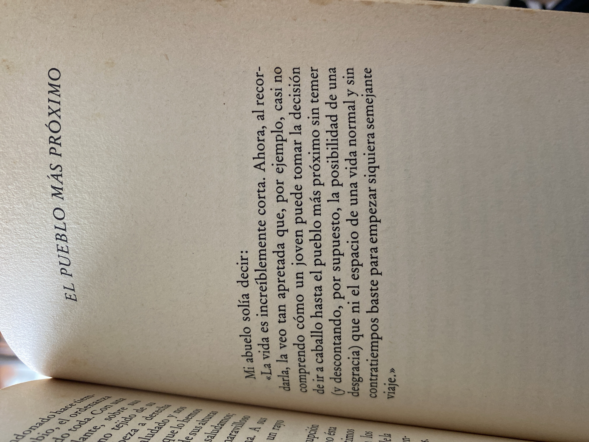 The image shows a book open to a page titled "EL PUEBLO MÁS PRÓXIMO". The text on the right-hand page is in Spanish and appears to be a quote from someone's grandfather, reflecting on how short and constrained life is and how daunting even a short journey can seem.