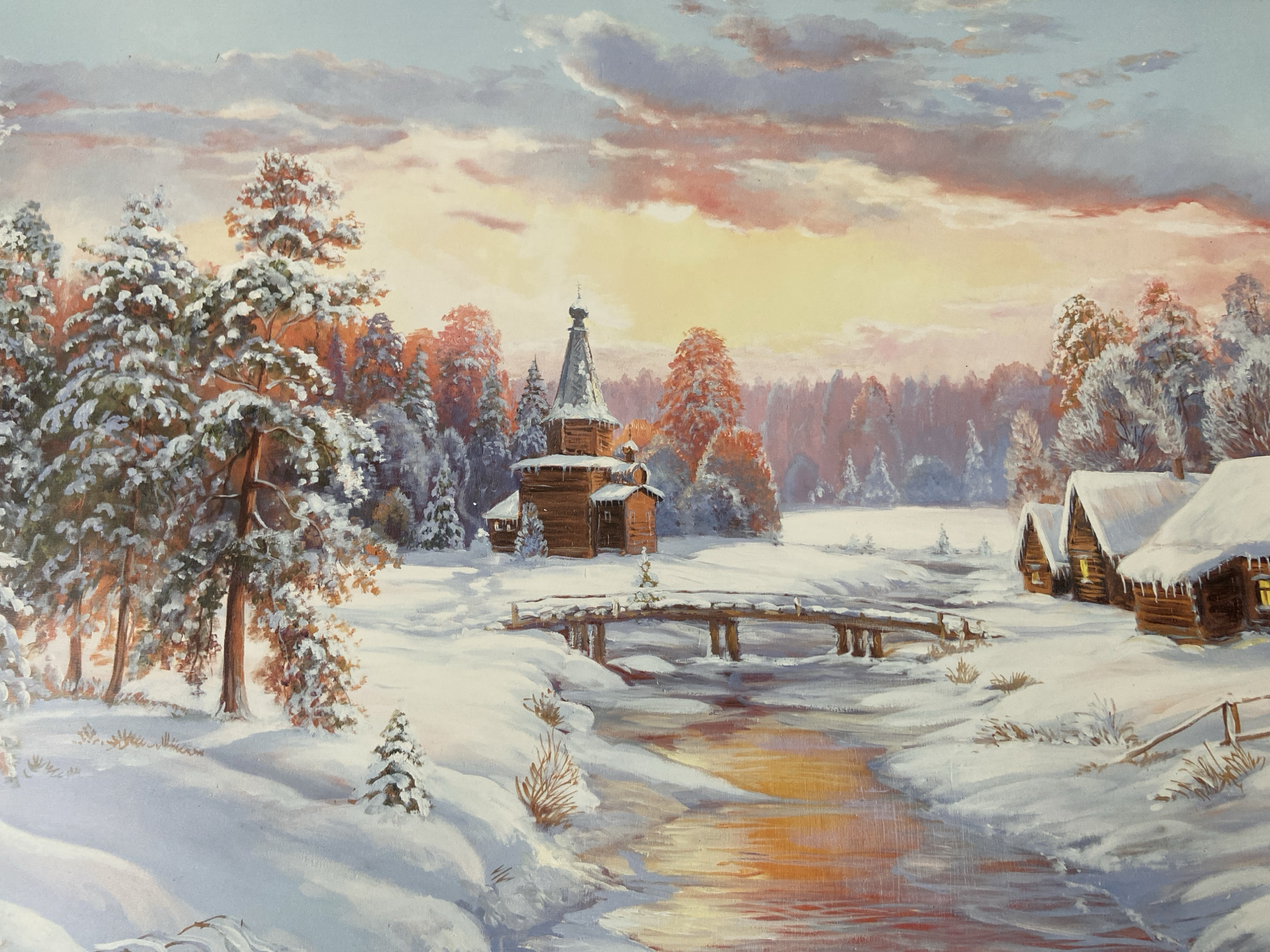 The painting depicts a serene winter landscape, likely in a rural area of Russia, with a focus on traditional wooden architecture and natural elements. In the mid-ground, a small, weathered wooden church with a dark, domed roof stands prominently. A rustic wooden bridge crosses a partially unfrozen stream in front of the church, reflecting the warm hues of the sunset. To the right of the stream, a row of charming log cabins with snow-laden roofs and illuminated windows suggests a small settlement. The surrounding environment is covered in a thick blanket of snow, with snow-dusted pine trees and other deciduous trees dotting the scene. The sky is painted with dramatic clouds tinged with the warm colors of a sunset, casting a soft, ethereal light over the entire landscape. There are no visible people in the scene. The overall impression is one of peaceful, untouched winter beauty, evoking a sense of tranquility and traditional rural life. The provided information about "Zamankul, Russia" is not visually verifiable from the image alone.