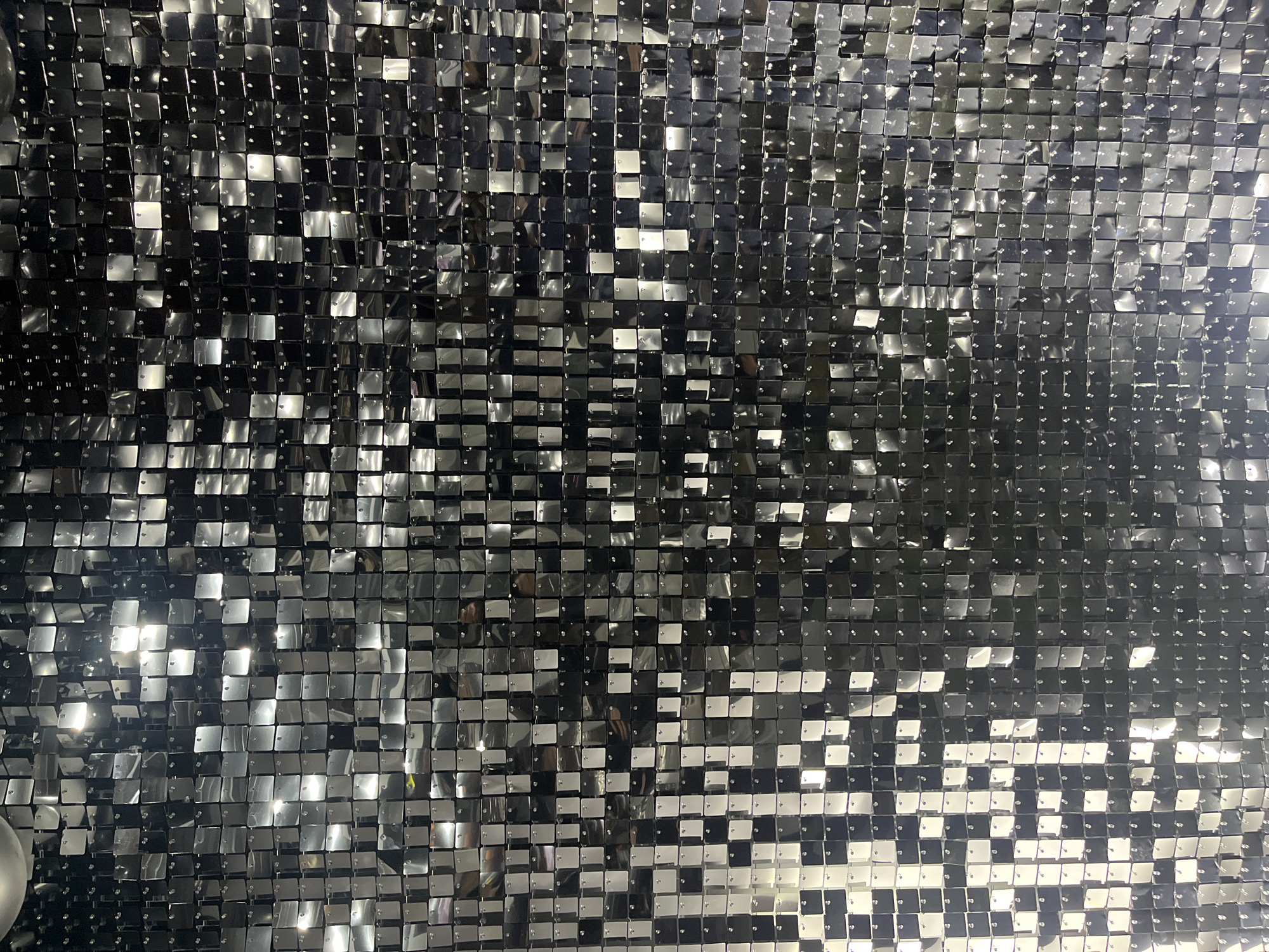 The image shows a dense wall of small, reflective silver squares. Each square appears to be slightly offset from its neighbors, creating a textured, shimmering surface. The overall effect is one of a mirrored, metallic curtain or backdrop. The location and any other details about the city of Goce Delcev, Bulgaria are not identifiable from the image.