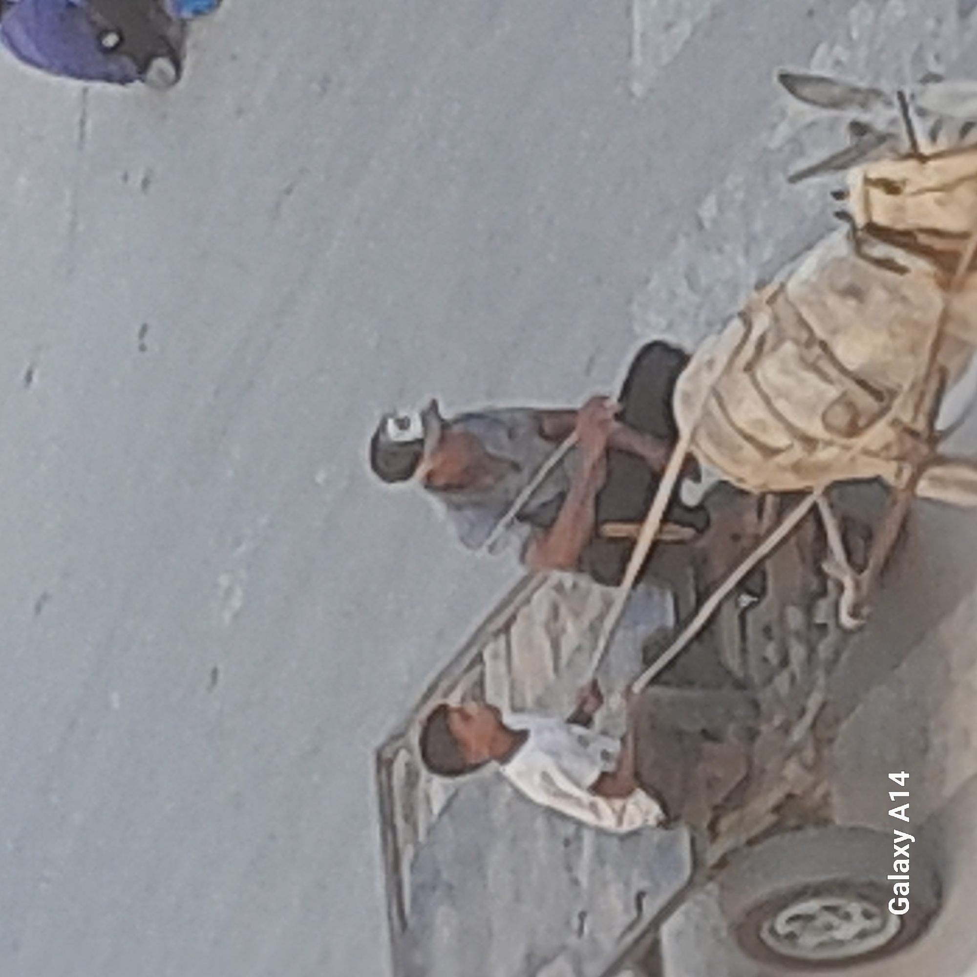 The image shows a scene in Khan Yunis, Palestinian Territories, where a donkey is pulling a cart. A young boy wearing a white t-shirt is seated in the front of the cart, and an older man wearing a cap and a light blue shirt is seated behind him. The cart appears to be loaded with materials wrapped in a tan-colored cloth. The ground is dirt or sand. The overall environment appears to be an outdoor urban or semi-urban setting, consistent with a location in Khan Yunis. The lighting suggests it is daytime.