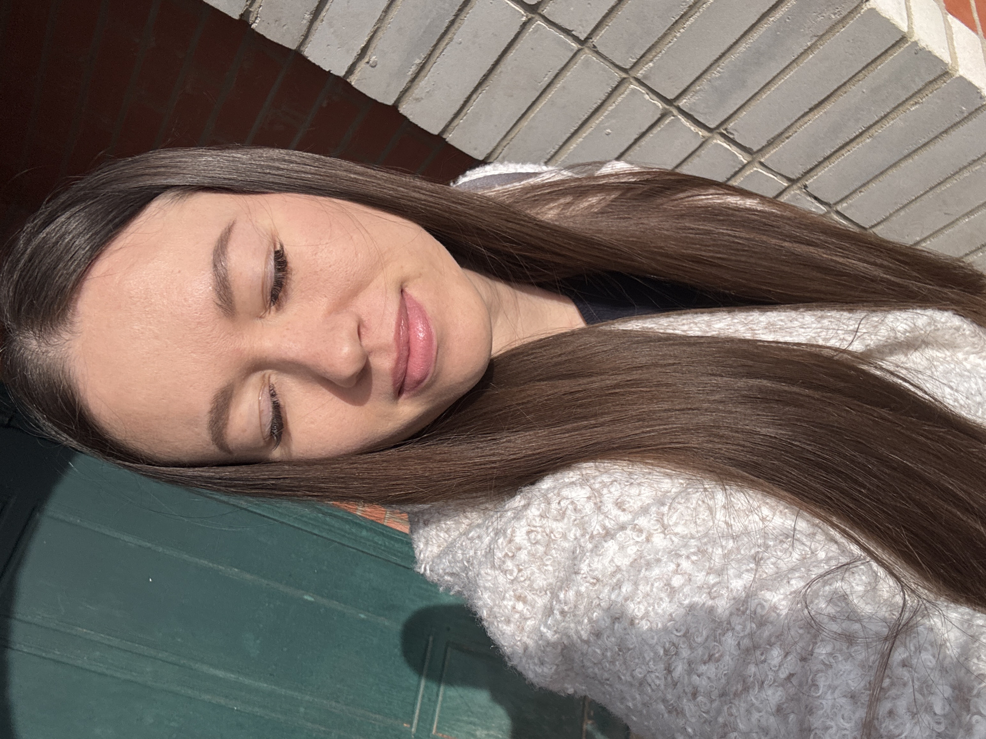 A woman with long brown hair and closed eyes lies on a textured surface that appears to be part of a door or wall. The background features a brick wall. The location is Ферма, Russia.