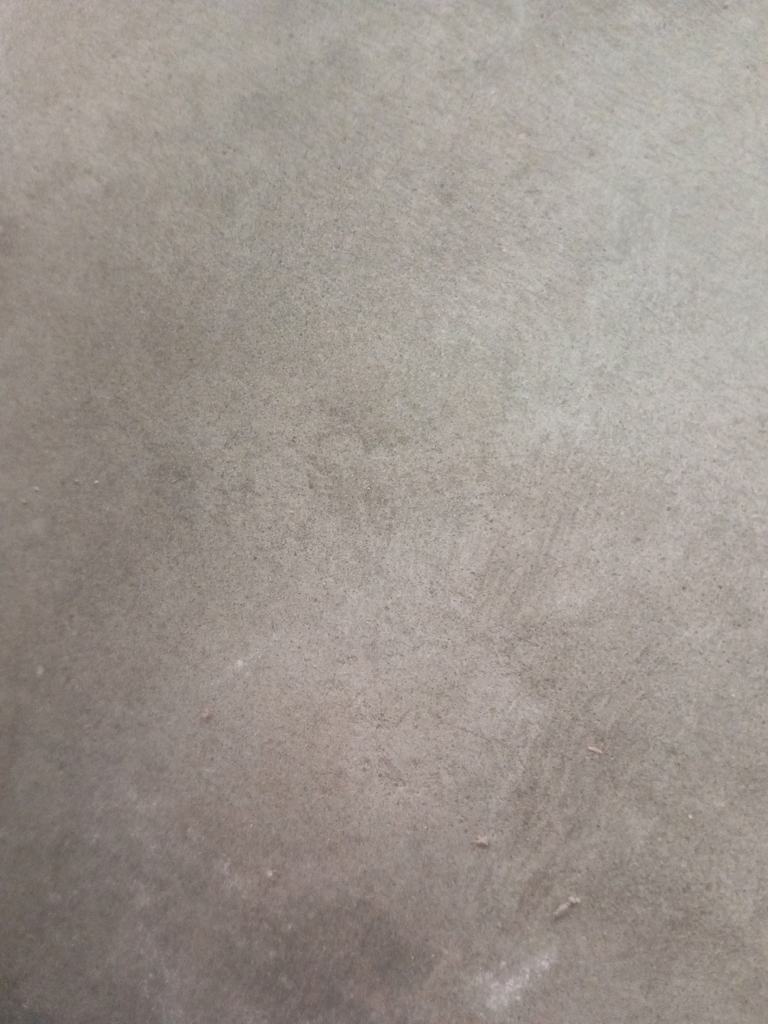 The image displays a close-up view of a textured concrete surface. The concrete is a neutral gray color with subtle variations in tone, suggesting a matte finish. There are no distinct objects or subjects visible in the image, and no discernible environmental features are present beyond the texture of the concrete itself. The scene appears to be an indoor or outdoor surface without any specific context provided by the image. No people, actions, or interactions are depicted. The location in Gambat, Pakistan is not visually represented within the image.