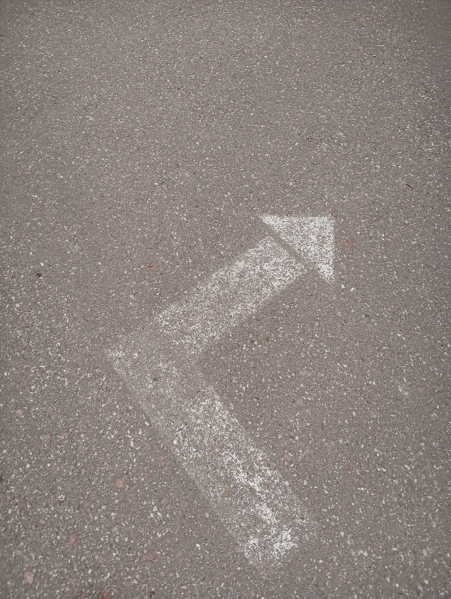The image shows an asphalt surface with a painted white arrow pointing upwards and slightly to the right. The arrow is faded and worn, suggesting it has been there for some time. The asphalt has a coarse texture, with small stones embedded in it. The location is likely in Poltava, Ukraine, but there is no specific information in the image to confirm this.