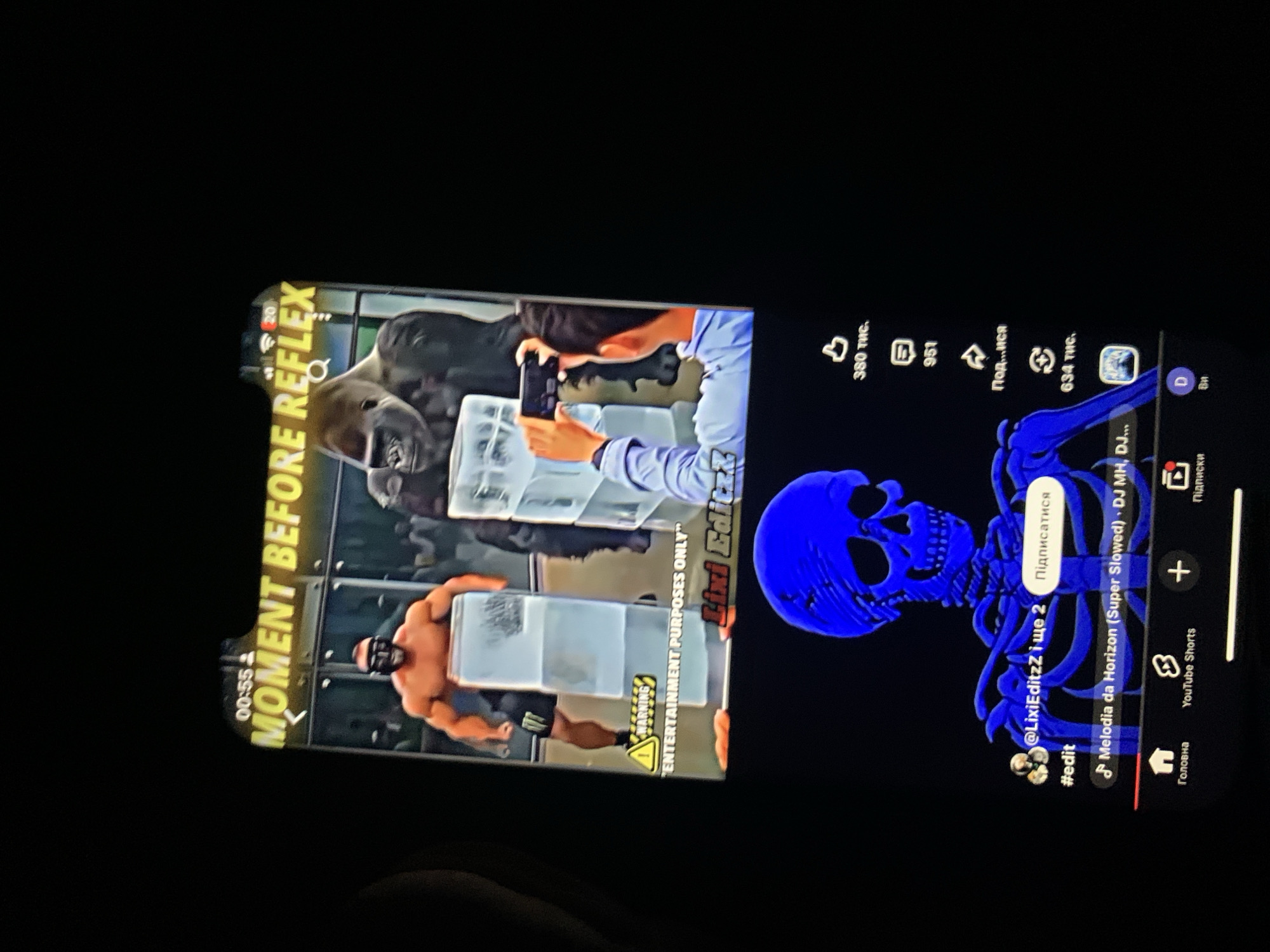 The image shows a close-up of a smartphone screen displaying a video. The video appears to be a short clip or meme with text overlaid. The top portion of the video shows a still image of a man in athletic wear holding a large ice block and a gorilla in the background. Text above the image reads "00:55 MOMENT BEFORE REFLEX". Below the image, there is a warning symbol and text that reads "ENTERTAINMENT PURPOSES ONLY". Further down, a username "@LixiEditzZ і ще 2" is visible along with a button that says "Підписатися" (which translates to "Subscribe" in Ukrainian). Below this, there is a hashtag "#edit" and music information: "Melodia da Horizon (Super Slowed) - DJ MH, DJ...". The lower part of the phone screen displays a bright blue skeletal figure. The phone is set against a dark background. There is no visible information linking this image or its content to the city of Zhmerynka, Ukraine.