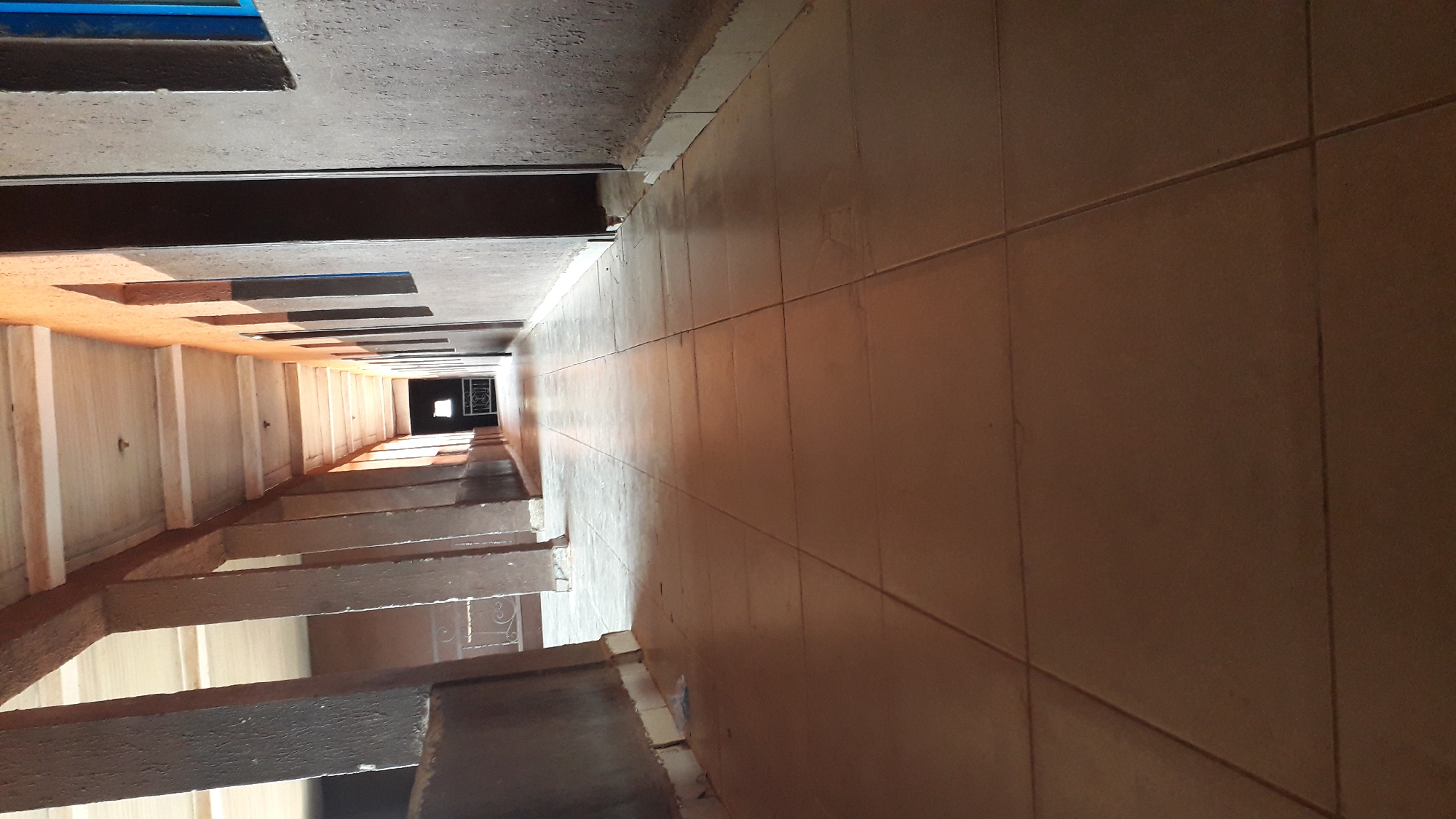 The image shows the interior of a stairwell in what appears to be a multi-story building. The stairs are visible on the left, with a series of steps ascending into the distance towards a window or opening at the end. The right side is dominated by a tiled wall. The stairwell appears to be in Onitsha, Nigeria.