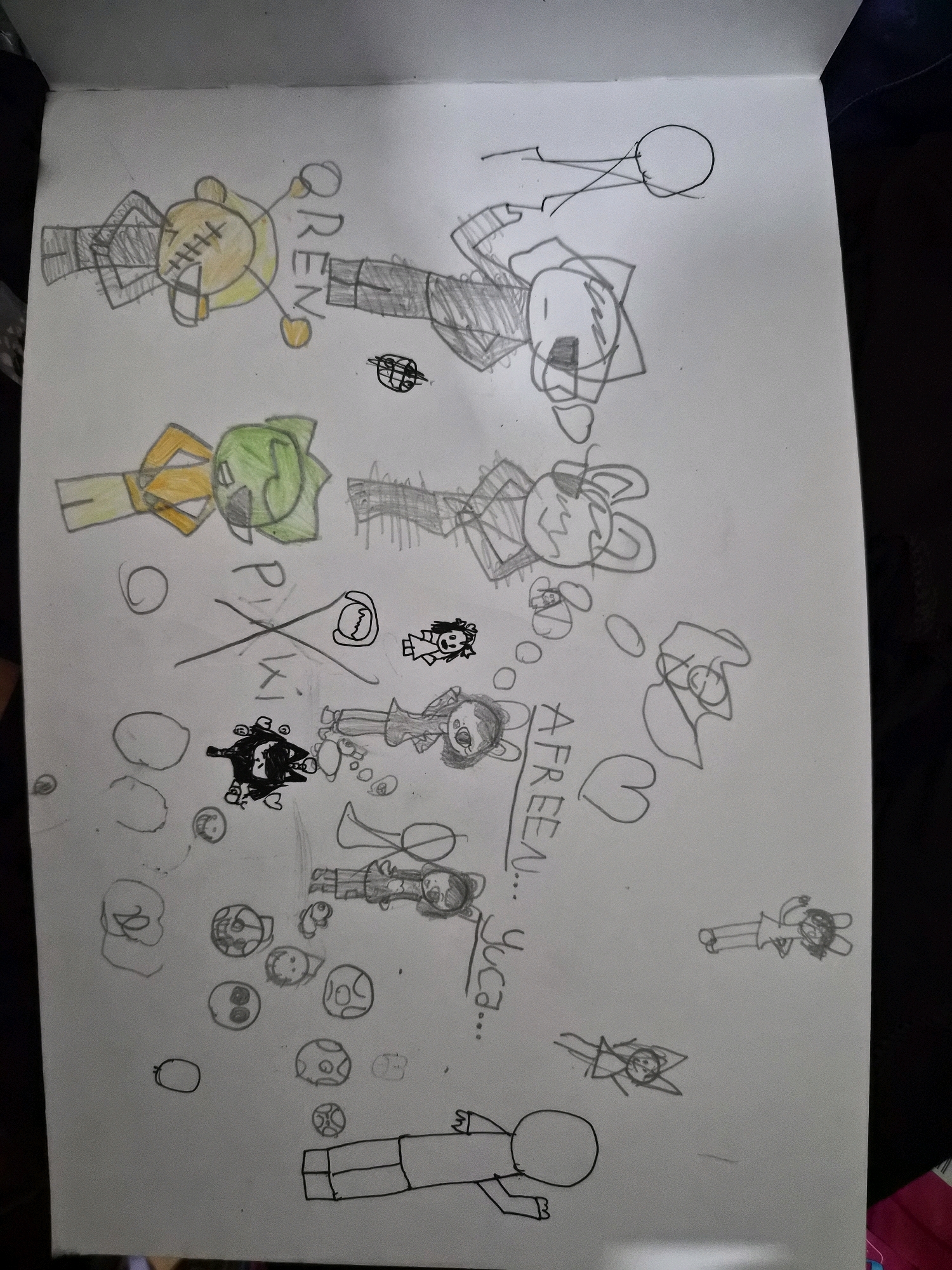 The image is a close-up, eye-level, slightly angled, full shot of a drawing on a white paper sketchbook. The drawing depicts several cartoon-like figures. In the upper left quadrant, there is a yellow figure with stitch marks on its face, wearing black pants, and the word "OREN" is written above it. To its right, there are two stick figures, one with a circle for a head, and another figure with a large head and ears. Below the yellow figure is a green figure with an orange shirt and black pants. To the right of the green figure is a grey, abstract figure with large ears. Below these figures, there are various smaller drawings, including a black blob-like creature with eyes and a small figure with a dress. There are also some scattered circles, hearts, and what appear to be mushrooms or balls. In the bottom center, there is a stick figure with a large circle for a head and an outlined body. Further down and to the right, there are several small figures with stick limbs. The phrase "AFREEN... YUCA..." is written vertically on the right side of the drawing. The background of the image is a dark, out-of-focus surface, possibly a table. There is no indication of the city of Balikpapan, Indonesia, or any urban environment.