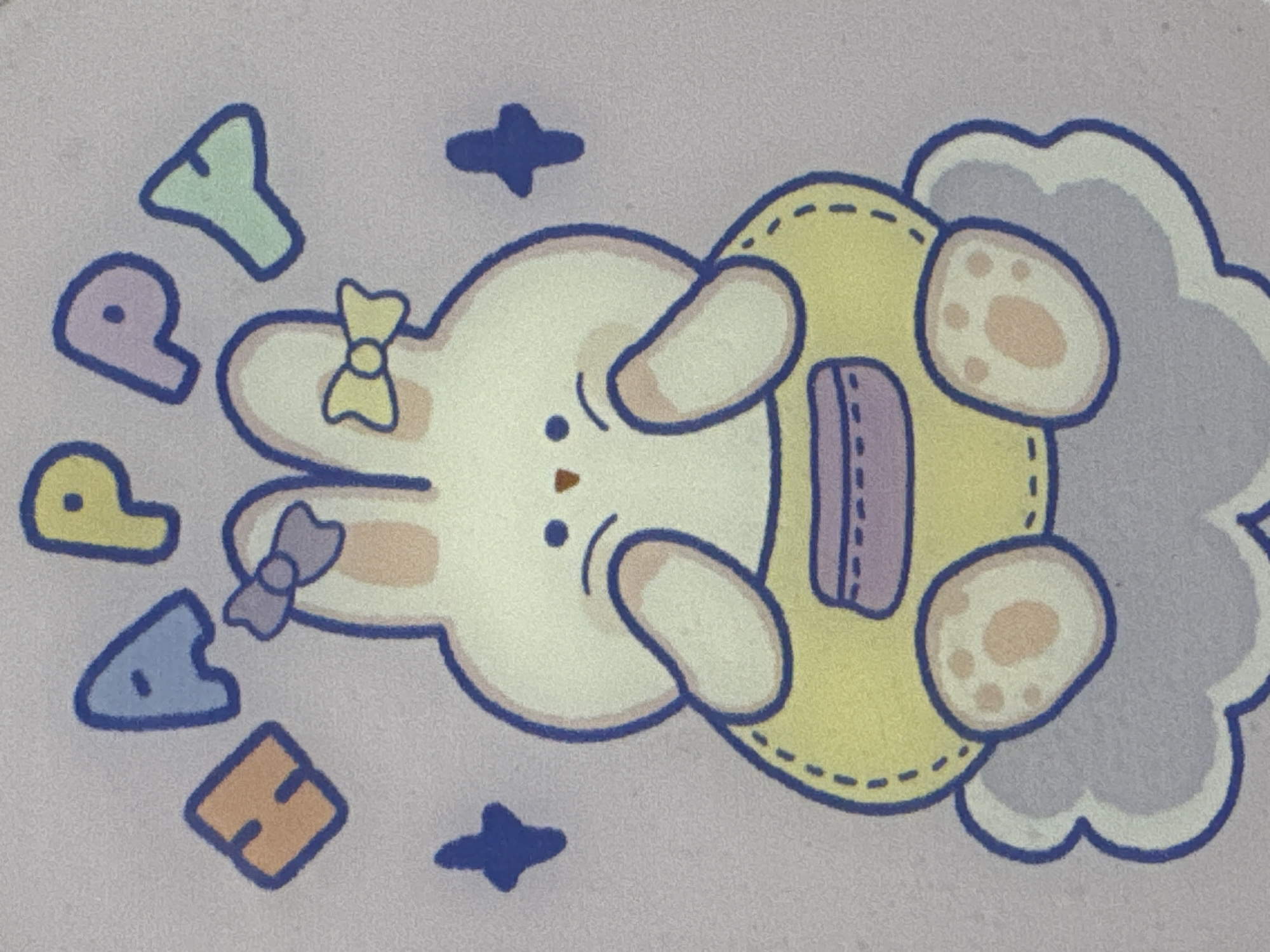 This media file features a charming, stylized cartoon rabbit character set against a plain, textured light lavender background. The rabbit, rendered in a creamy white hue with a dark blue outline, is depicted lying on its back. It has small dot eyes and a tiny brown nose, and appears relaxed or content. Two small bows adorn its ears: one light yellow on its upper ear and one light purple on its lower ear.
The rabbit wears a yellow, overall-style garment with dashed stitching and a light purple rectangular detail on its chest, possibly a pocket or strap. Its paws are visible, showcasing light peach-colored pads. A soft, light blue-grey cloud-like shape partially frames the rabbit on its right side.
Scattered around the rabbit, predominantly on its left, are five colorful, block-style letters, each outlined in dark blue. These letters, arranged vertically, spell out "HAPPY": an orange "H", a light blue "A", a light purple "P", a light yellow "P", and a light green "Y". Two small, dark blue star-like shapes are also visible near the rabbit.
The overall scene conveys a playful, cheerful, and innocent mood, characteristic of children's illustrations or decorative art. The image itself does not provide specific location or time-of-day cues; however, it is associated with Saint Petersburg, Russia, based on the provided context.