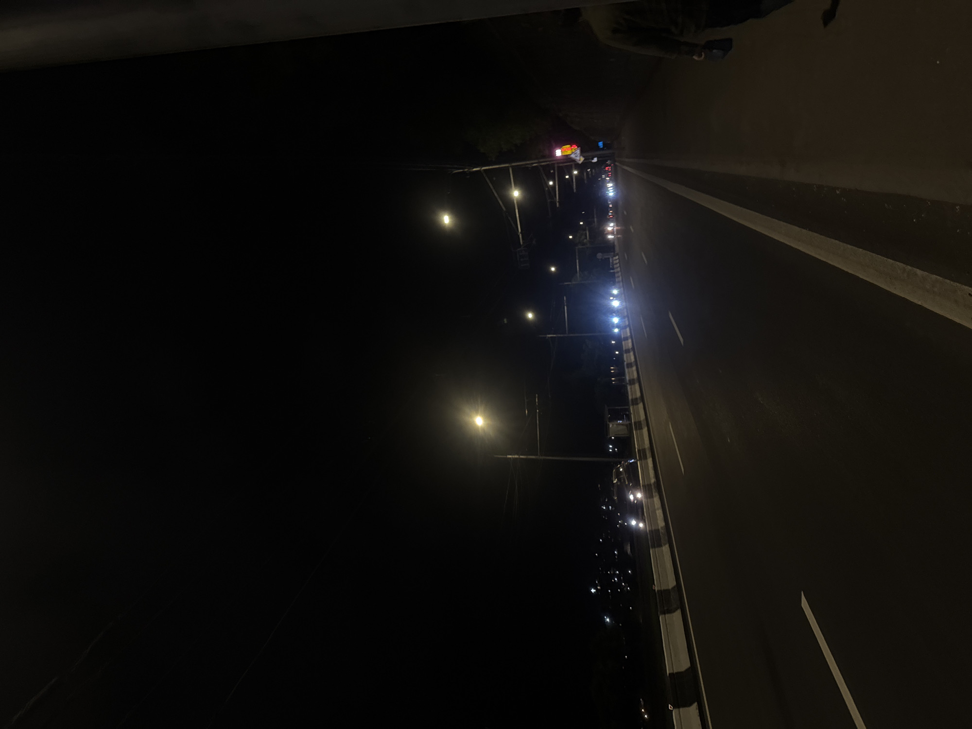The image depicts a nighttime view of a road in Yerevan, Armenia. Streetlights illuminate the roadway, with cars visible in the distance. The road has white lane markings and is bordered by concrete barriers. The photograph is taken from an elevated position, possibly a bridge or overpass. The overall scene is dark with a sense of urban stillness.