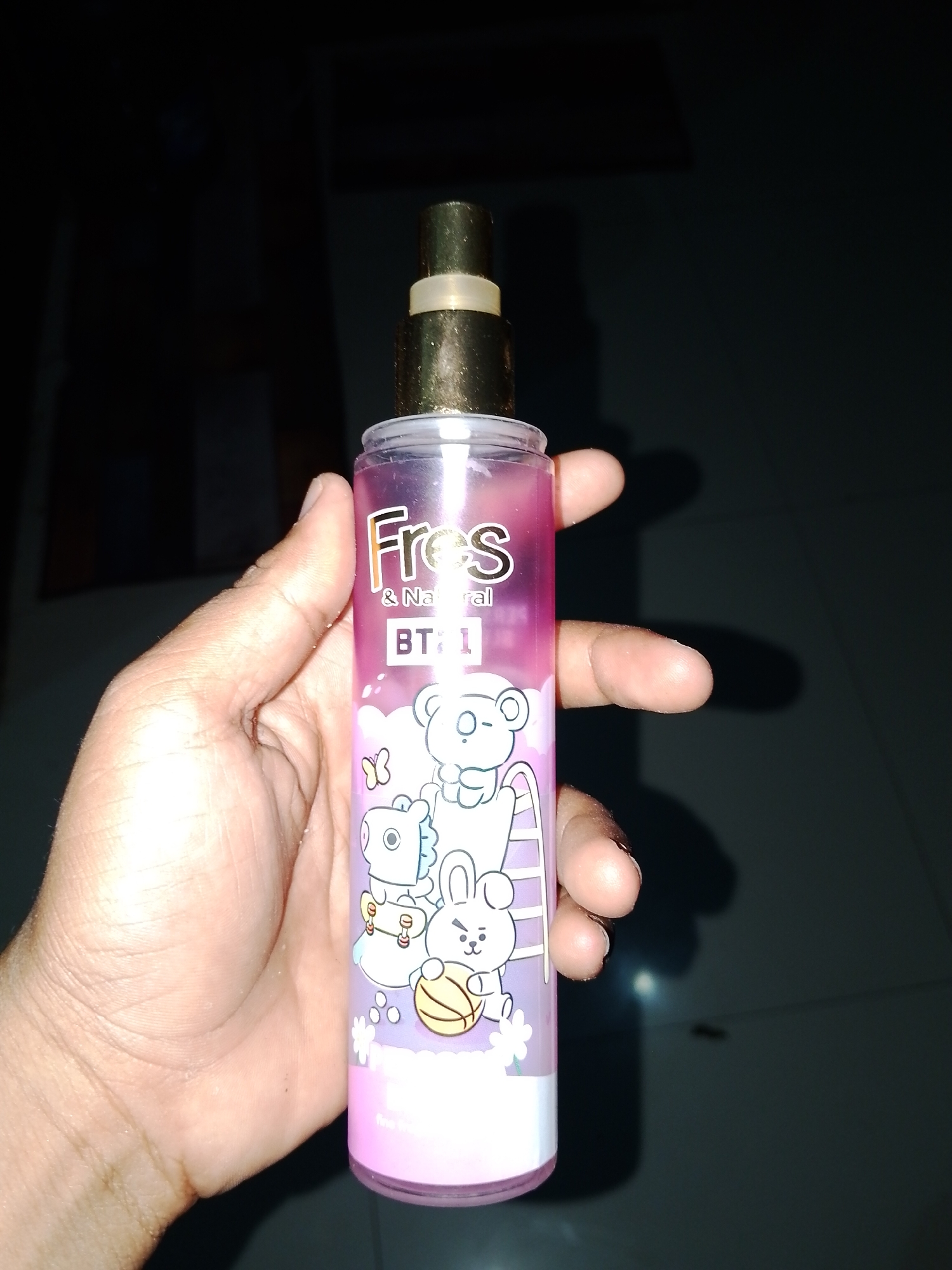 A hand is holding a pink spray bottle with a gold cap and a white ring. The bottle has cartoon characters on it, including what appears to be a white bear and a white rabbit holding a basketball. The text on the bottle reads "Fress & Natural BT21". The background is dark, suggesting the photo was taken indoors or at night. The specific location in Sendangrejo, Indonesia, is not discernible from the image itself.