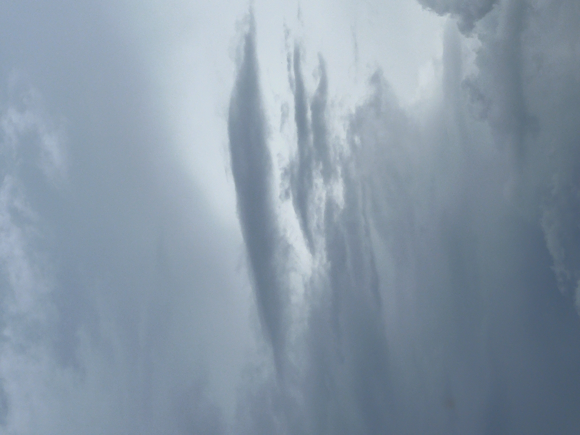 The image shows a cloudy sky over Warsaw, Poland. The clouds are gray and appear to be low in the sky, suggesting the possibility of rain or overcast weather. The lighting is diffused, with no direct sunlight visible. The overall atmosphere is somber and subdued. There are no people or objects visible in the image, only the sky and clouds.