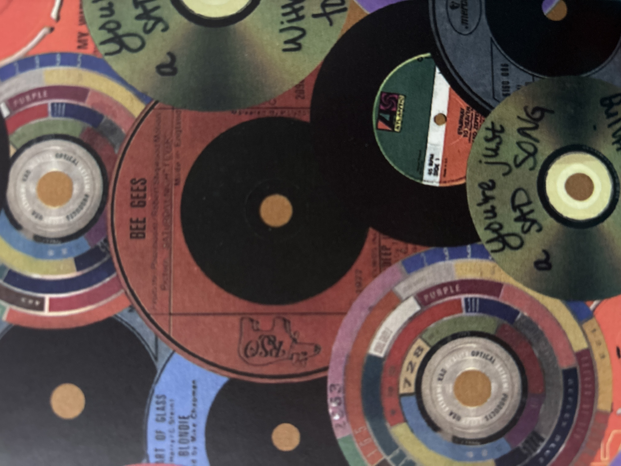 The image shows a collage of vinyl records and record labels. Some records have handwritten text on them. Brands and artists like "Blondie," "Bee Gees," and labels like "RSO" and "Atlantic" are visible. The labels are colorful, with some featuring intricate designs or segmented color wheels. I have no information to link this image to Votkinsk, Russia.