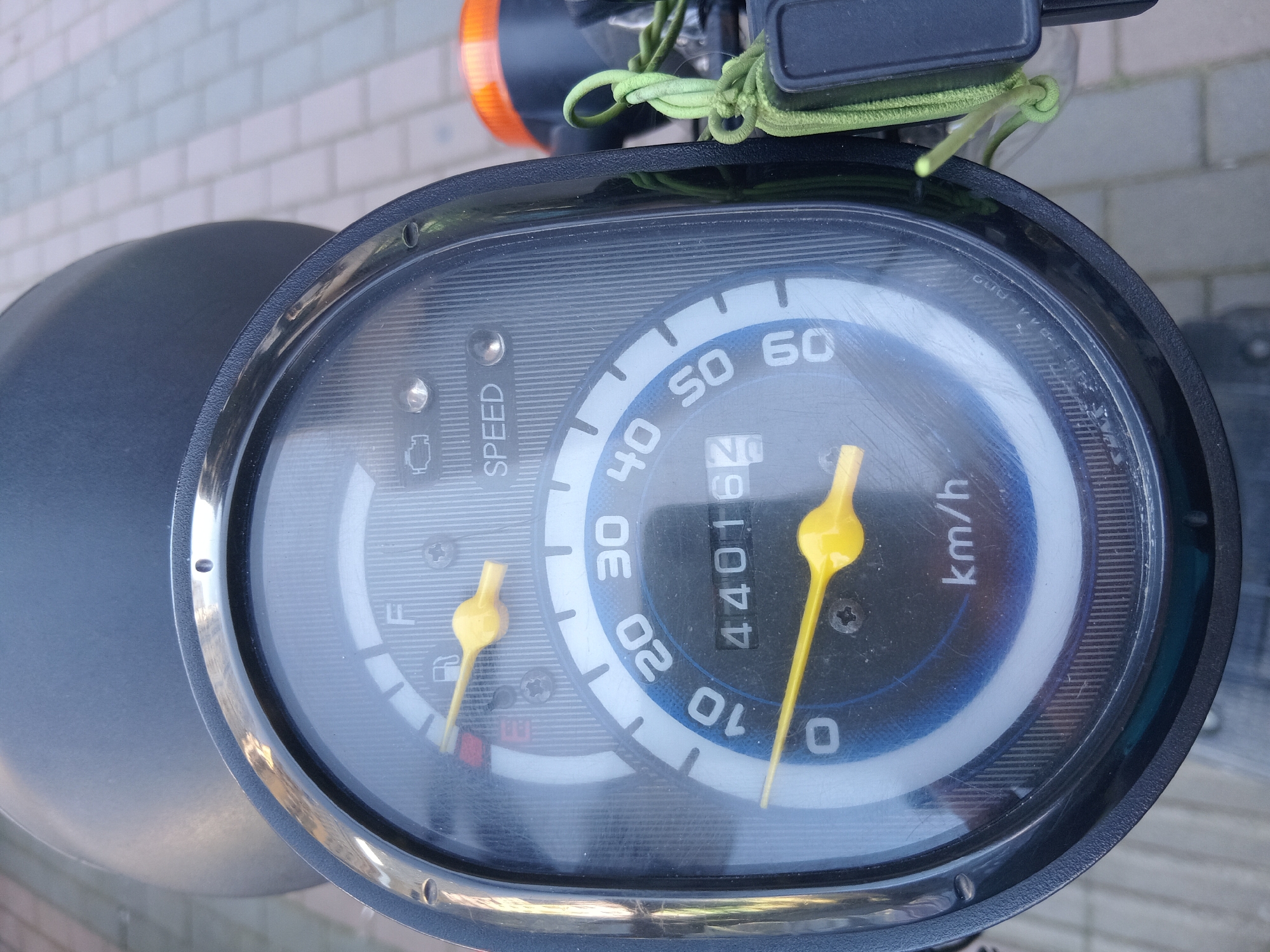 The image shows the speedometer of a scooter. The speedometer reads 44016 km. The fuel gauge indicates that the fuel tank is nearly empty. The needle on the speedometer indicates the scooter is going 10 km/h. The background suggests that the scooter may be in Batumi, Georgia. The background is a grey and tan brick sidewalk.