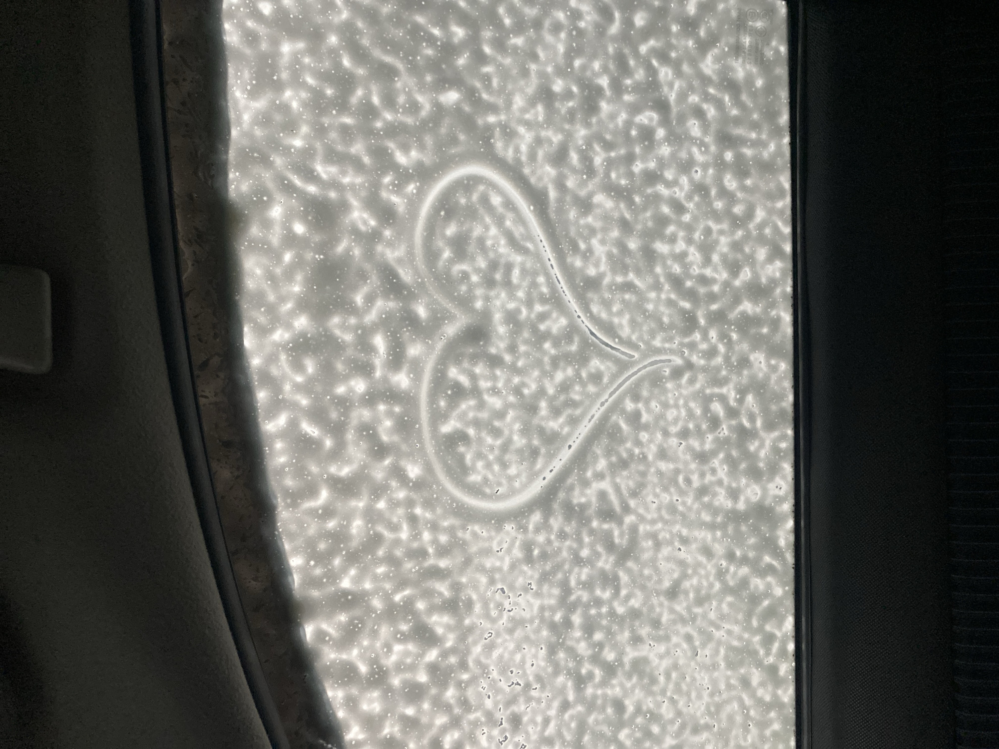 The image shows a view through a car window covered in soap suds, likely at a car wash. A heart shape has been drawn in the soap on the glass. The interior of the car is visible on the left and right edges of the frame. The location in Votkinsk, Russia is not identifiable from the image.