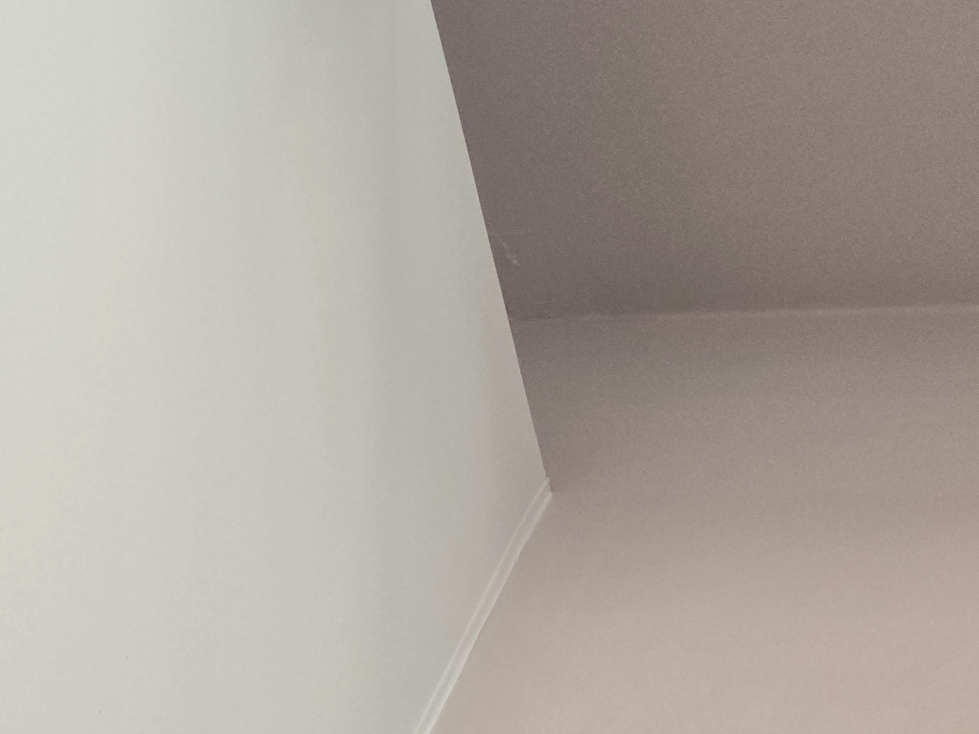 The image shows a close-up view of a corner where a white ceiling meets a mauve-colored wall. A decorative molding runs along the junction of the ceiling and the wall. There is a faint scuff mark on the wall near the corner. The lighting appears to be from an artificial source, casting subtle shadows and highlighting the textures of the painted surfaces. The scene is indoors, likely in a residential or commercial building. No people or specific objects are visible beyond the architectural elements. The location of Ulan-Ude, Russia is not determinable from the visual information provided in the image.